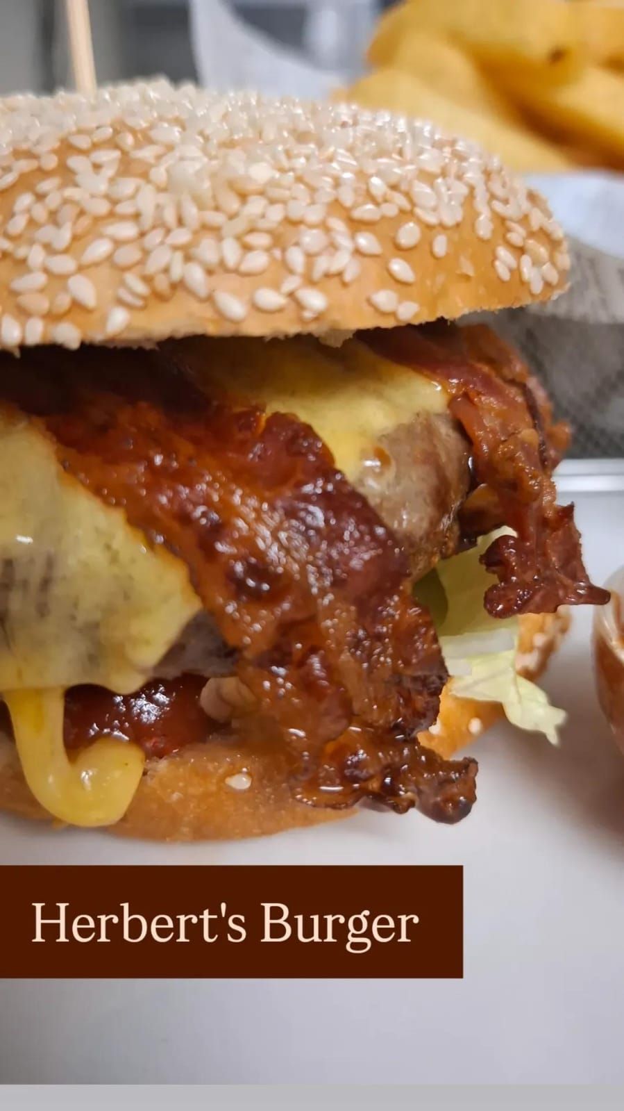 Közelkép egy szezámos zsemlével, olvasztott sajttal és ropogós baconnel díszített hamburgerről.