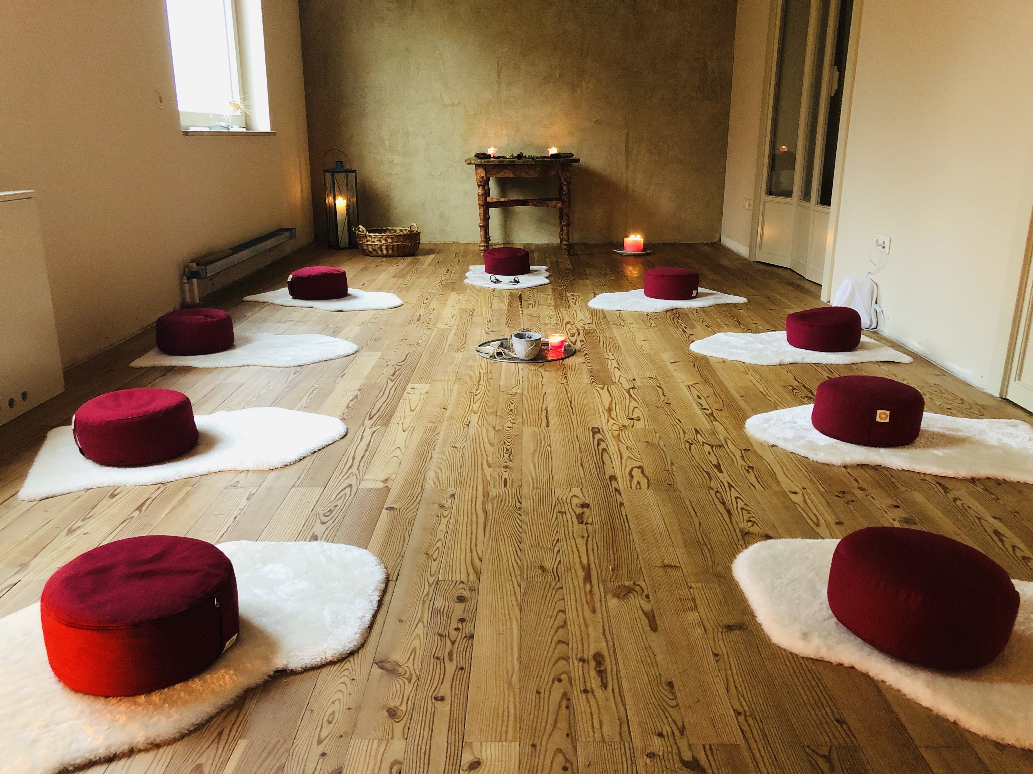 Meditációs szoba fehér szőnyegeken elhelyezett piros párnákkal, gyertyákkal és fapadlóval.
