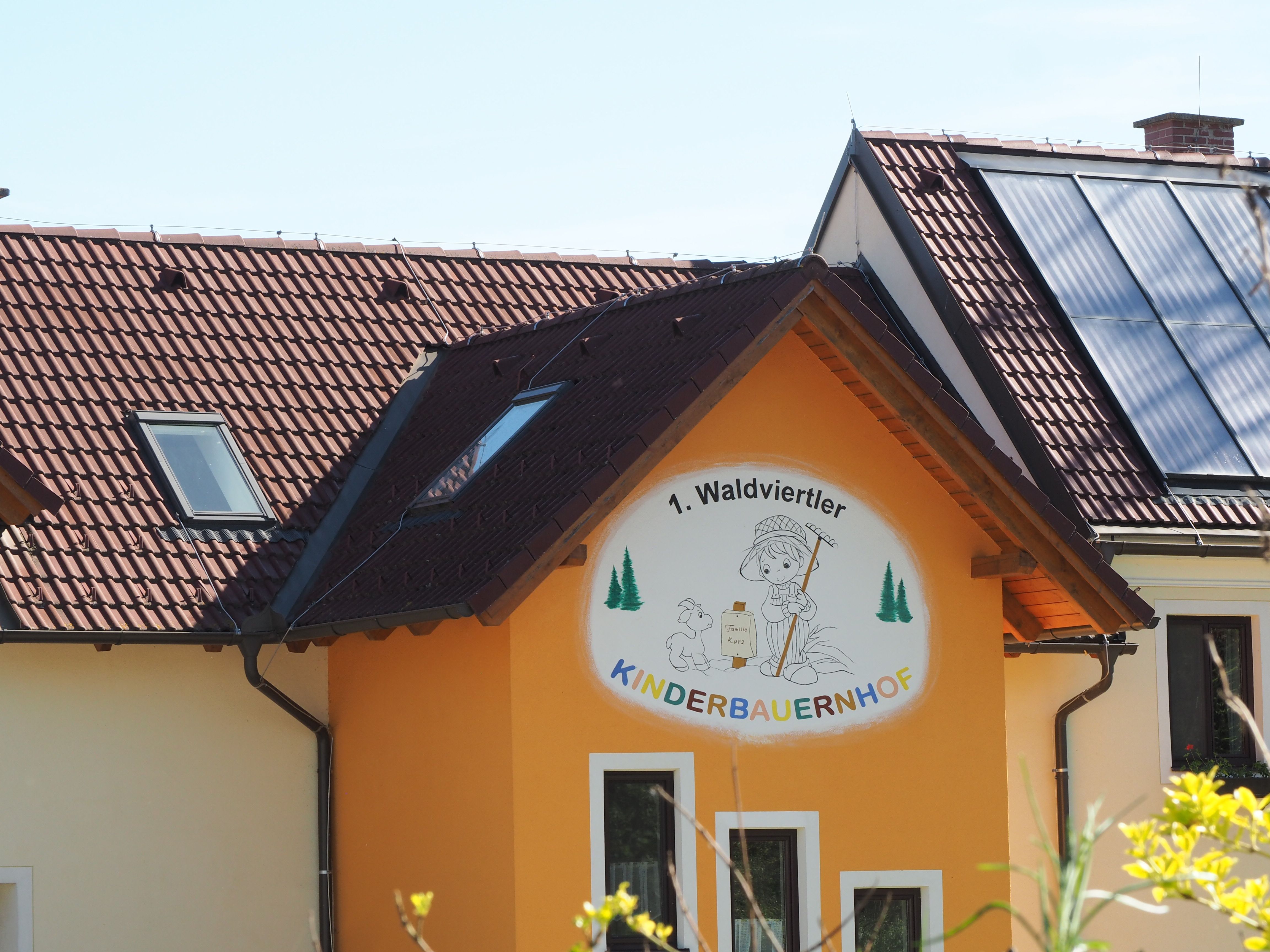"1. Waldviertler Kinderbauernhof" feliratú épület, napelemek a tetőn.