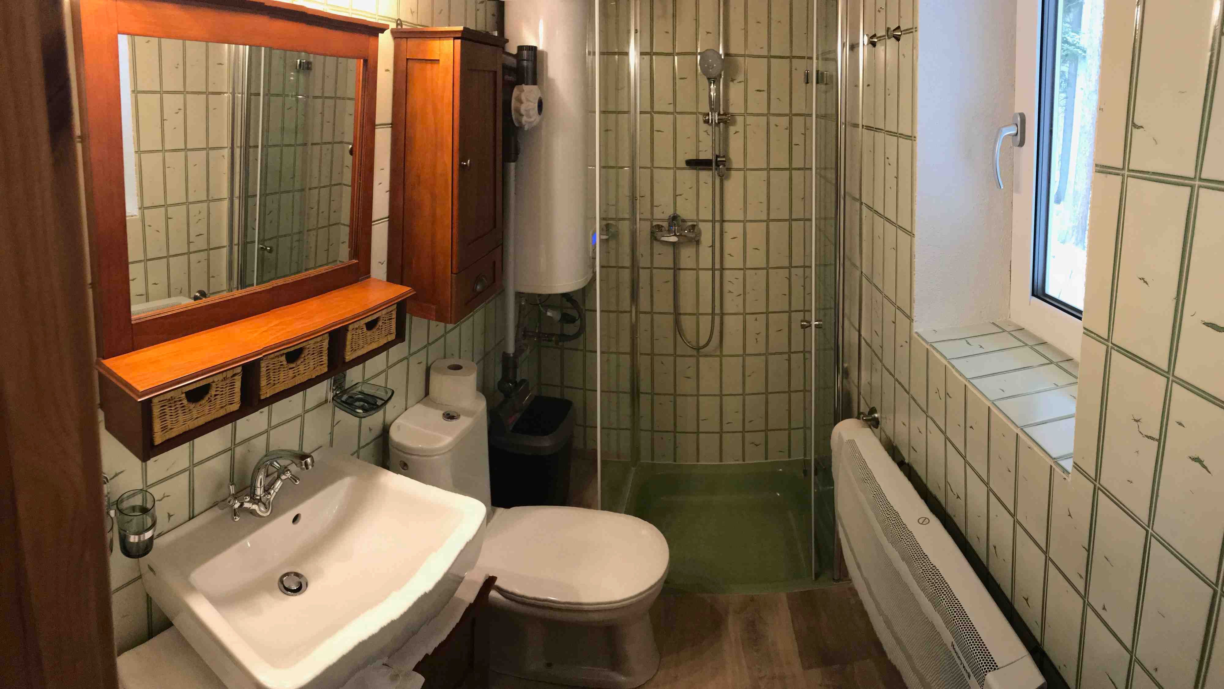 Kis fürdőszoba zuhanyzóval, mosdóval, WC-vel és fa szekrényekkel.