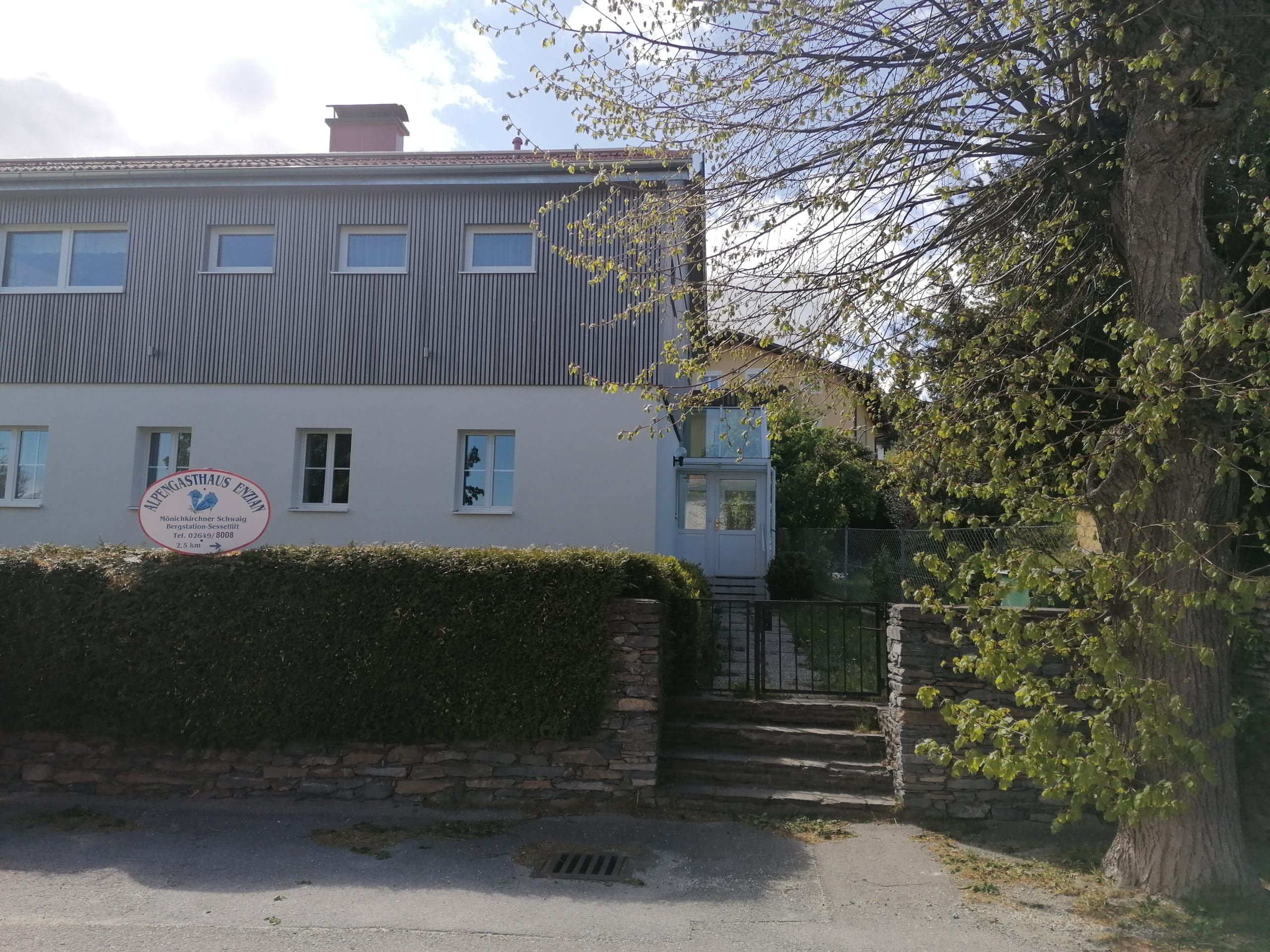 Kétszintes épület "Alpengasthaus Ewin" felirattal és kerttel.