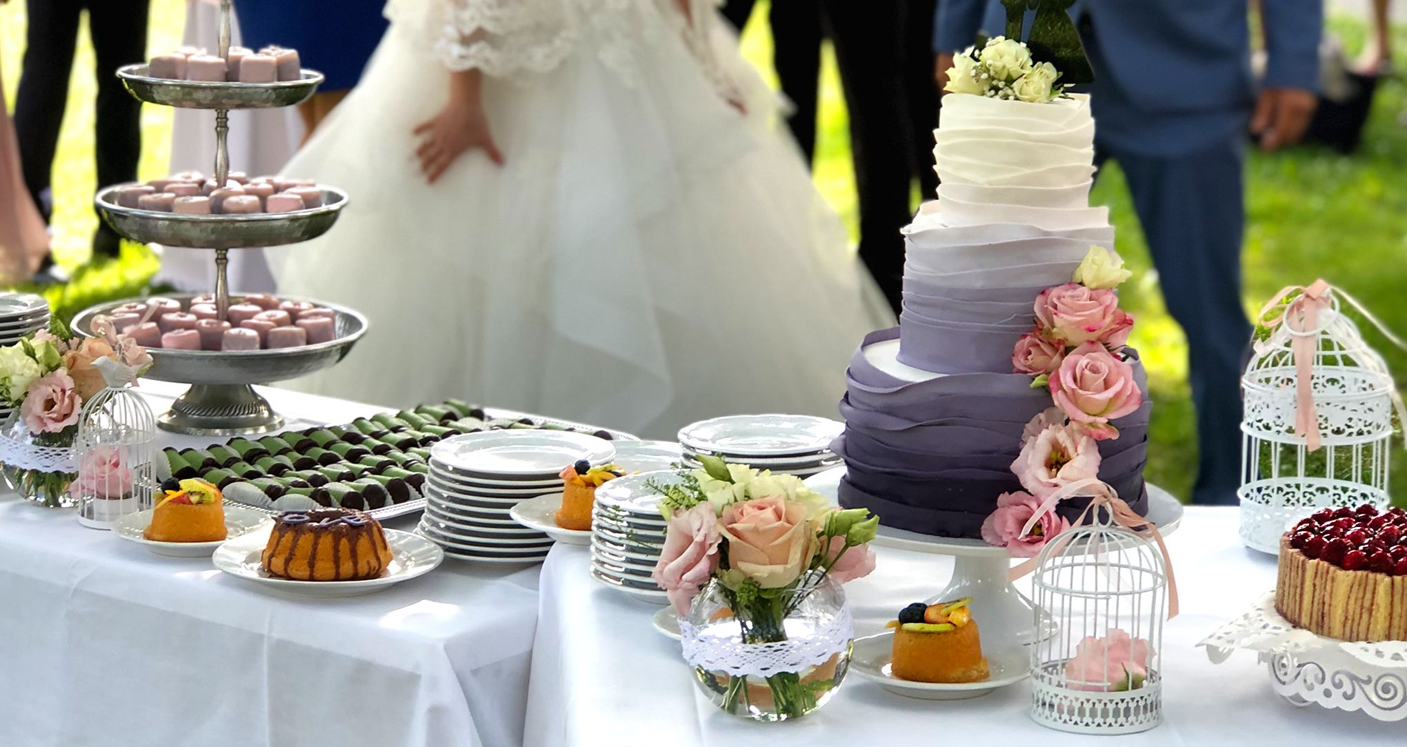 Esküvői torta és desszertek egy szabadtéri asztalon a menyasszonnyal és a vőlegénnyel.