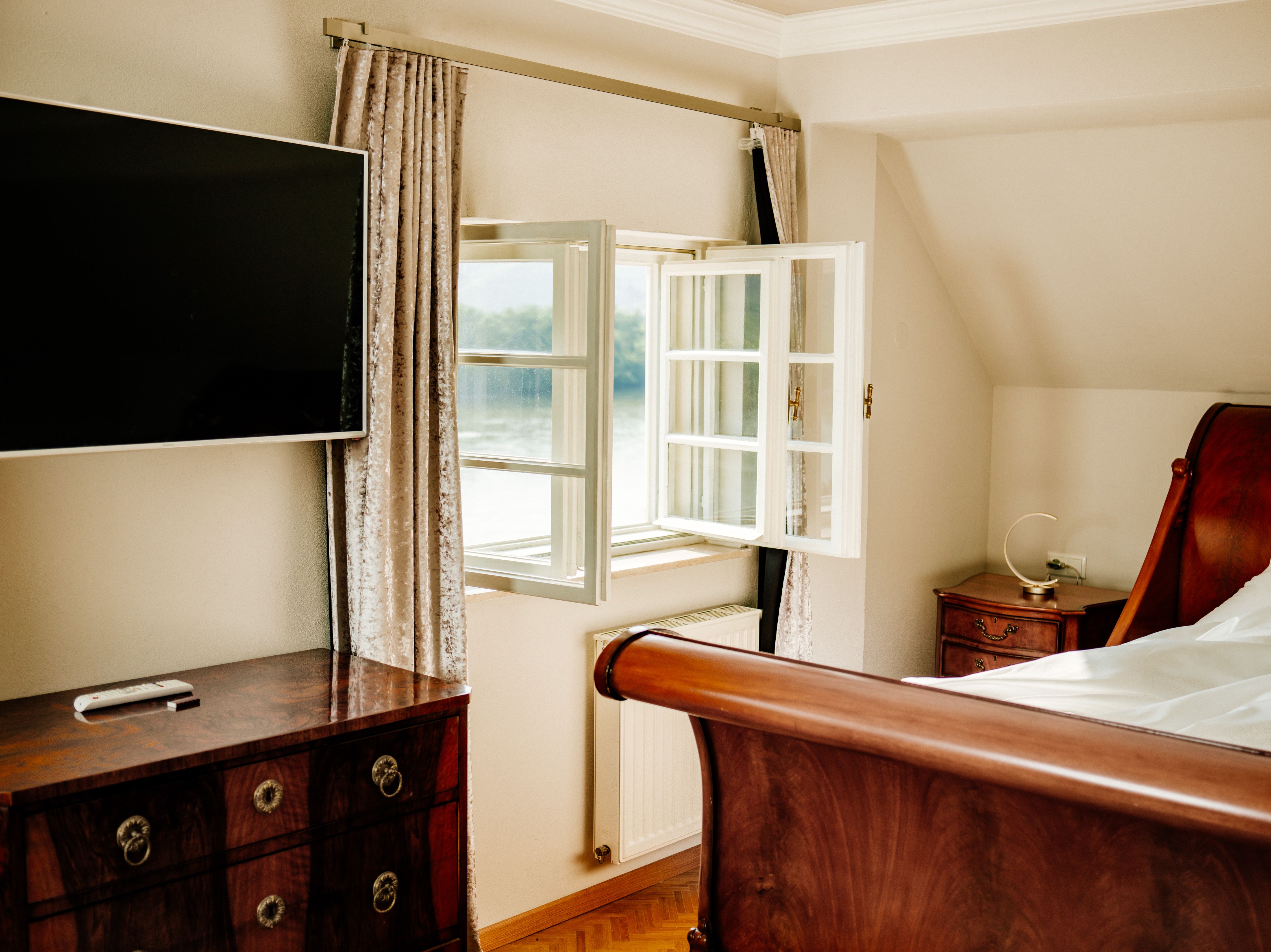 Elegáns hálószoba nyitott ablakkal, síkképernyős TV-vel, faággyal és antik bútorokkal.