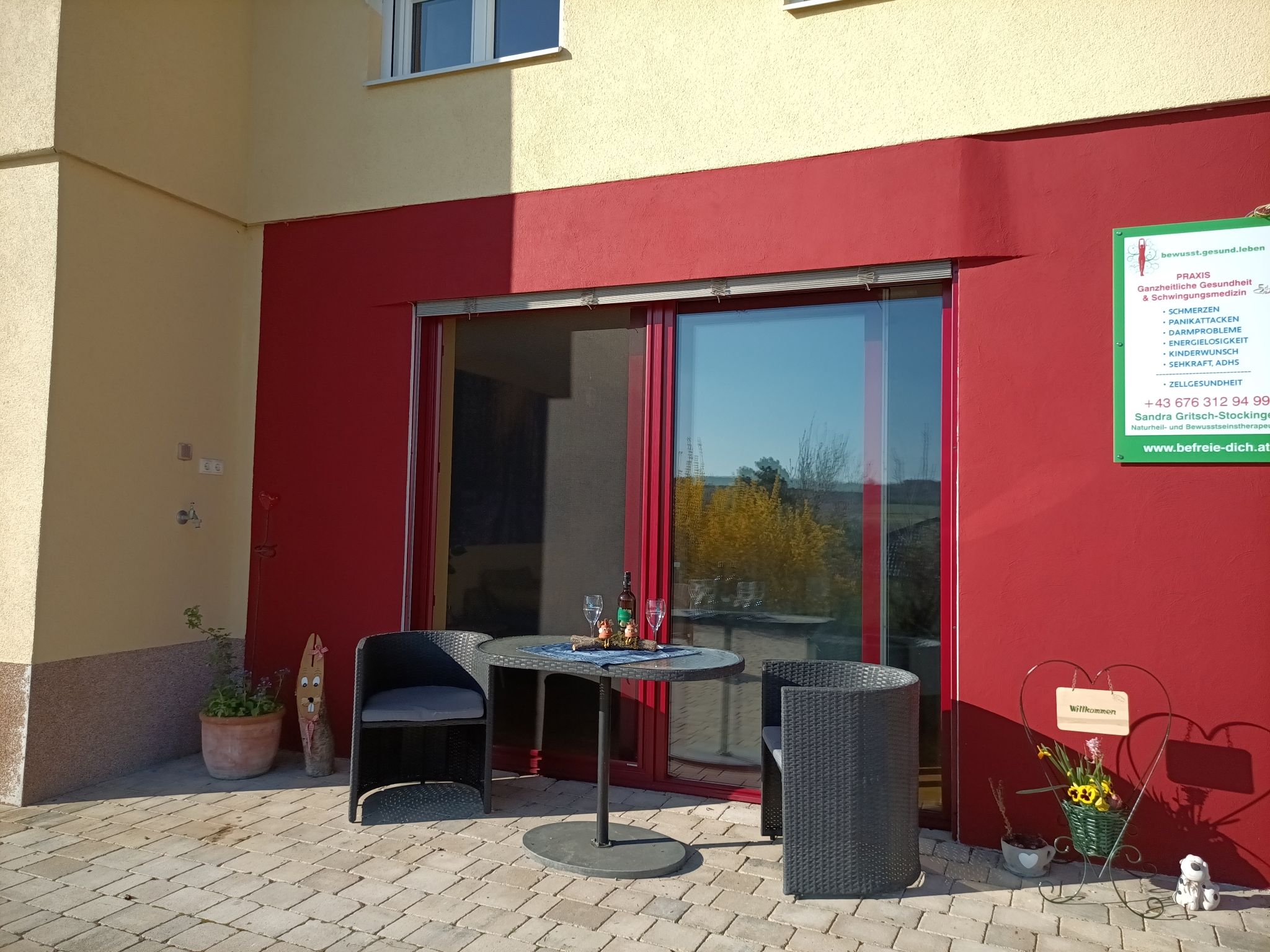 Terasz két székkel és egy asztallal egy piros fal előtt, mellette egy tájékoztató tábla.