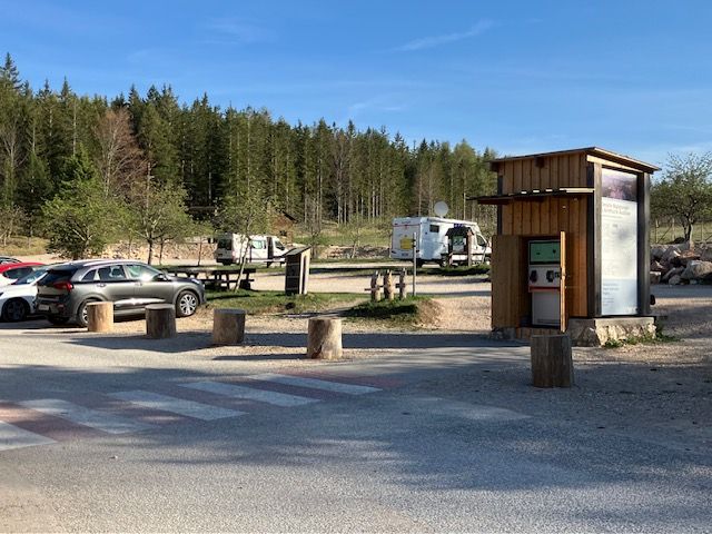 Parkoló a Hohe Wand Natúrpark Központnál személygépkocsikkal és lakóautókkal, erdővel körülvéve.