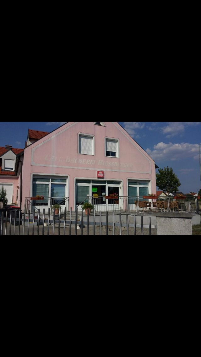 A "Bäckerei-Café Hiessberger" feliratú rózsaszín épület külső nézete. Az épület előtt asztalok és székek állnak.