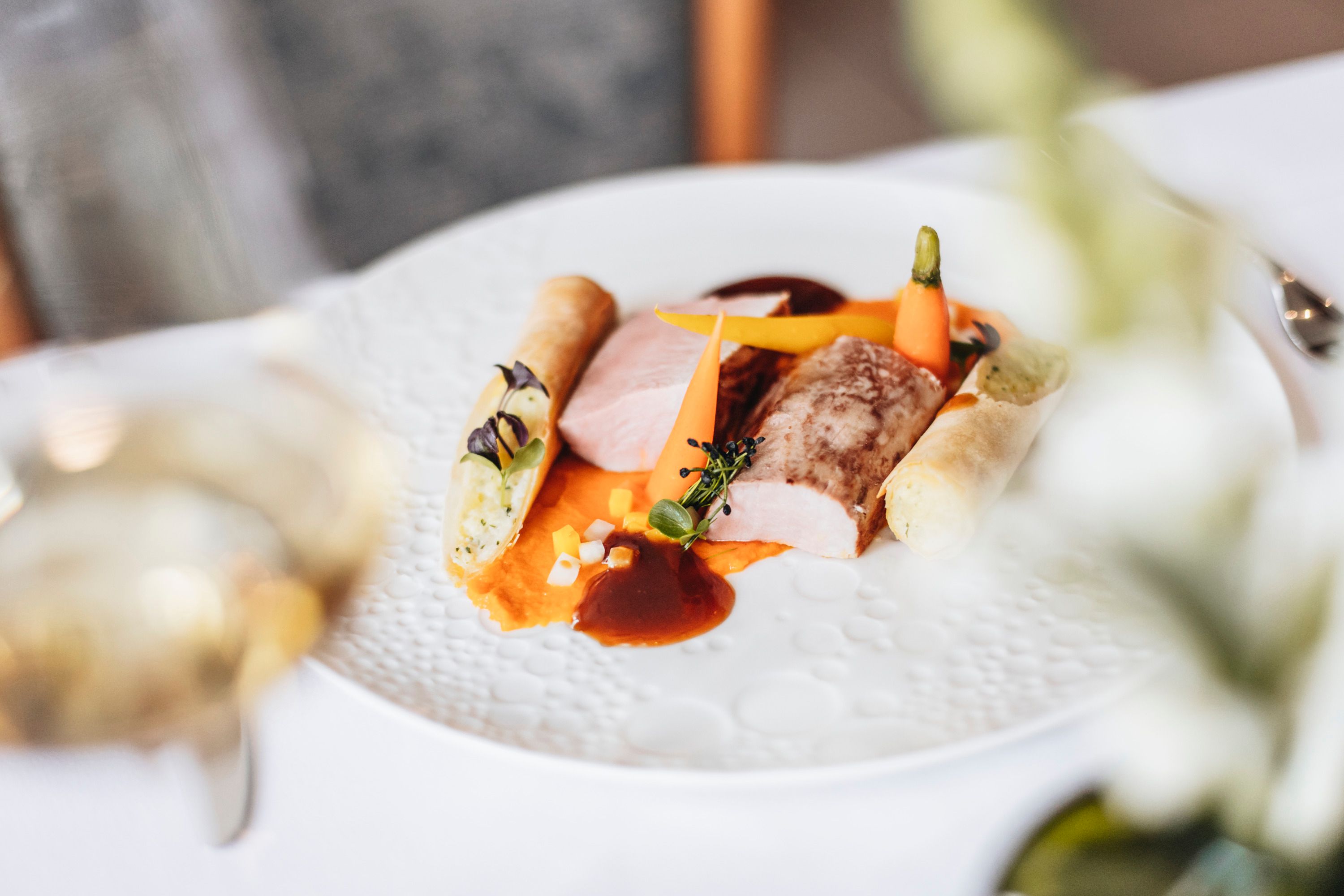 Ínyenc étel sertésfilével, zöldségekkel és burgonyatekerccsel fehér tányéron.