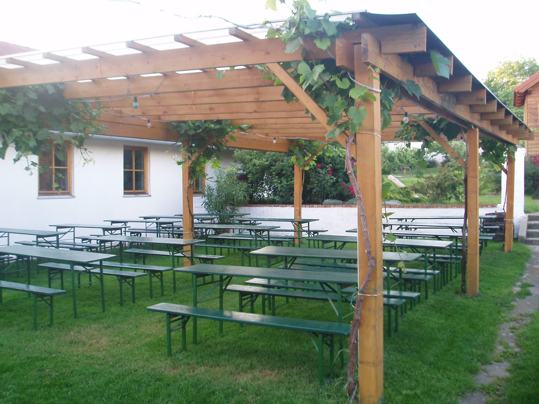 Sörkert fapadokkal és asztalokkal egy szőlővel borított pergola alatt.