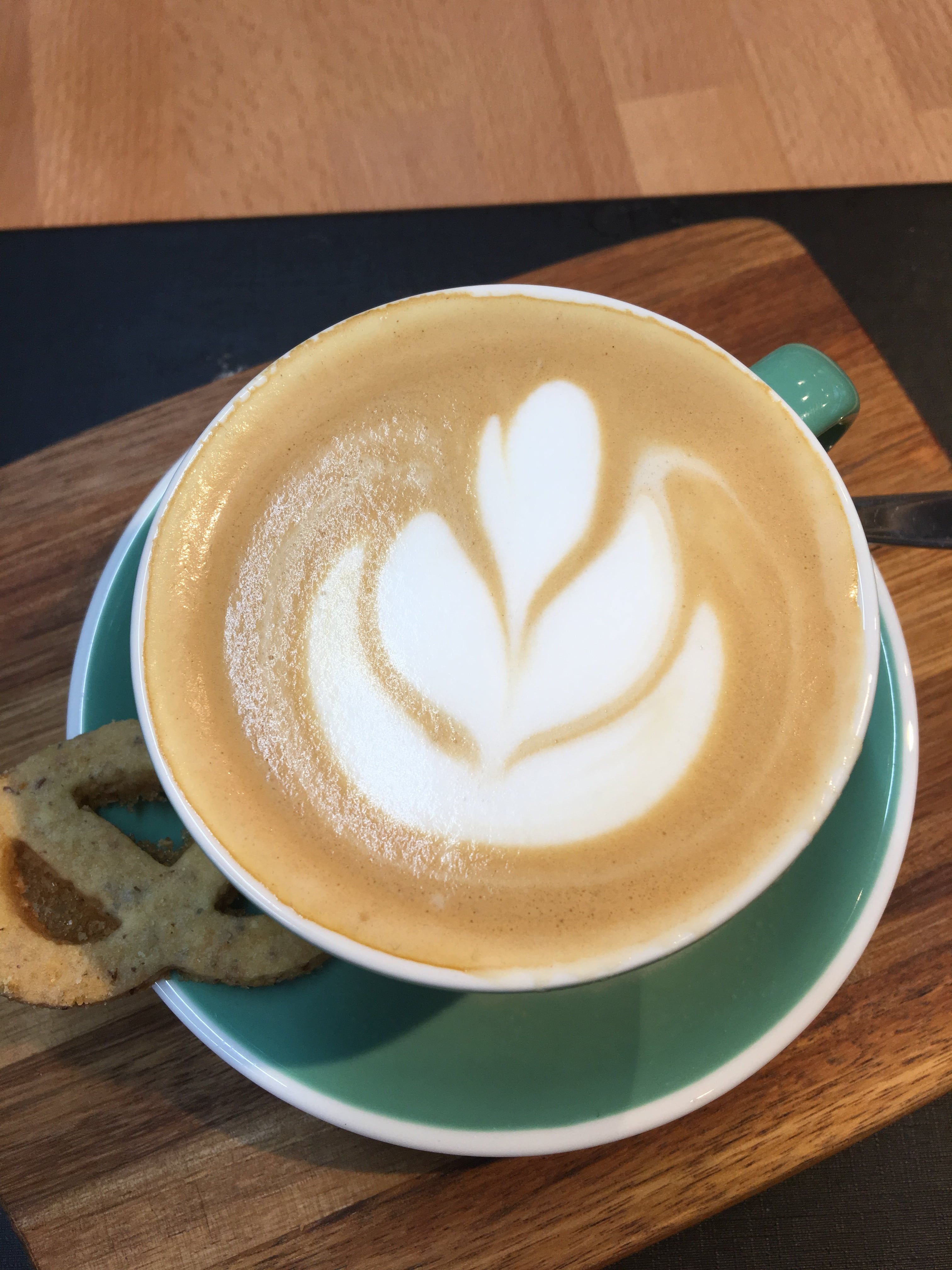 Kapucsínó latte arttal zöld csészében, fatáblán.