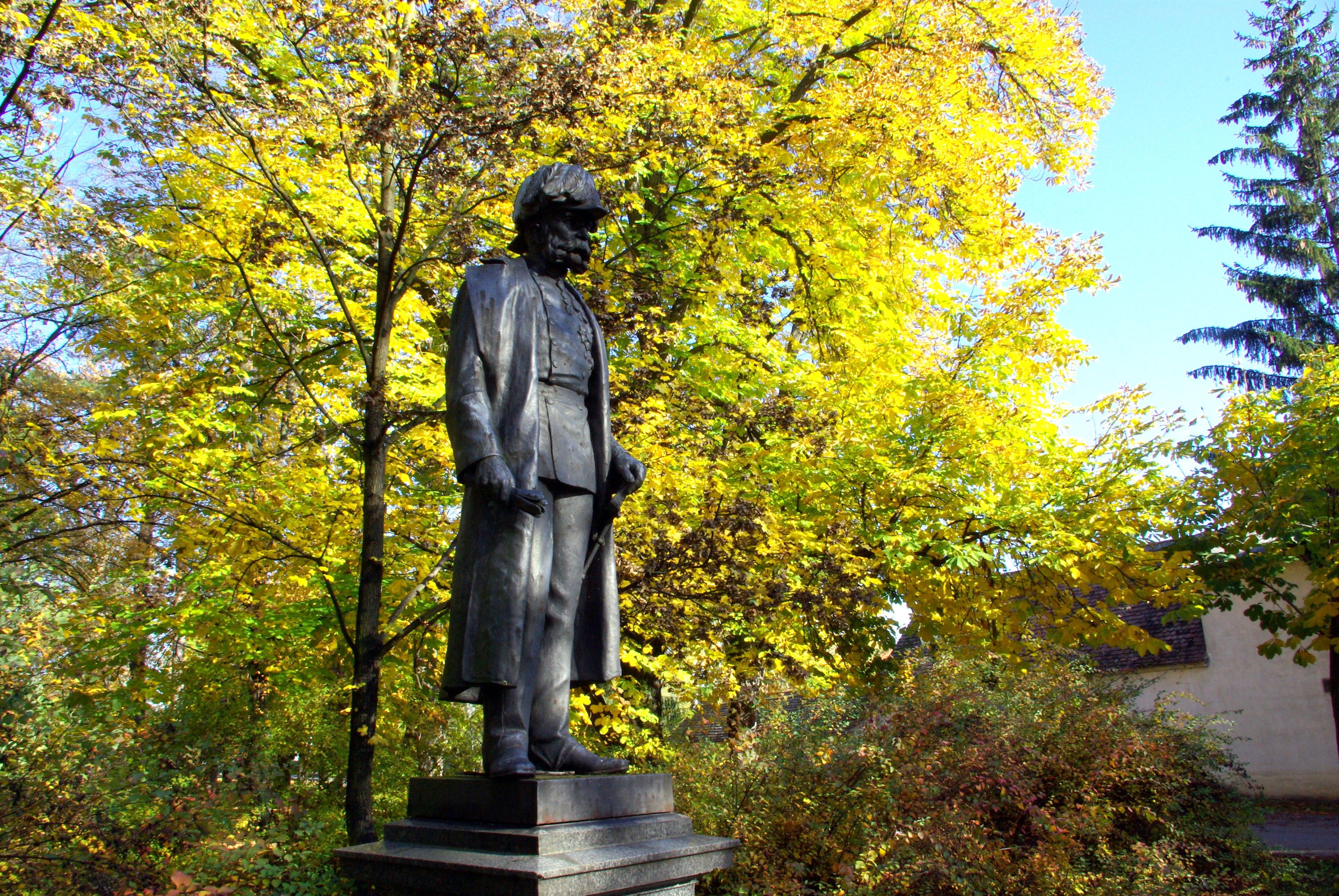 Egy férfi szobra egy őszi parkban, háttérben sárga levelekkel.