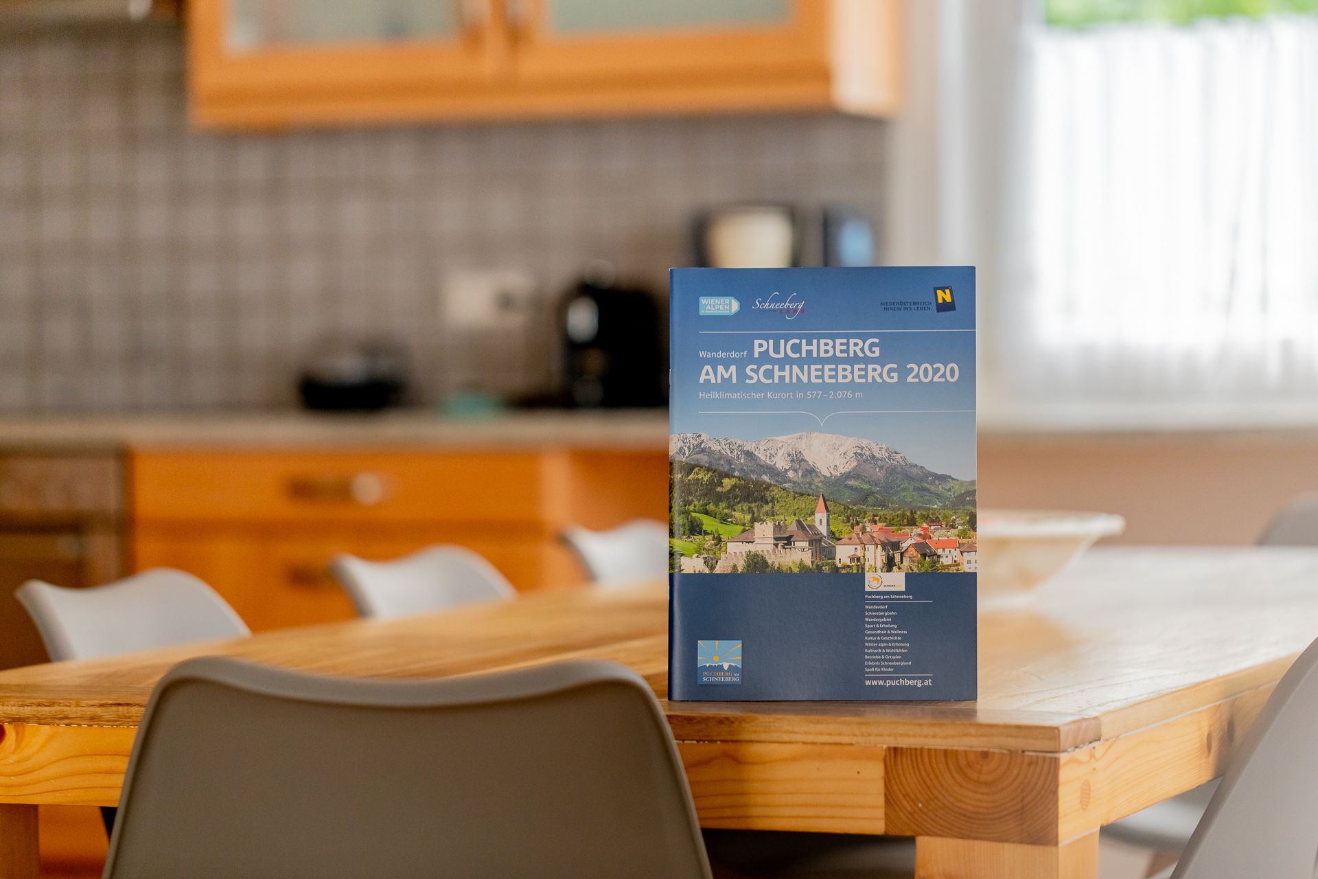 Egy konyhai faasztalon egy Puchberg am Schneebergről szóló brosúra áll.
