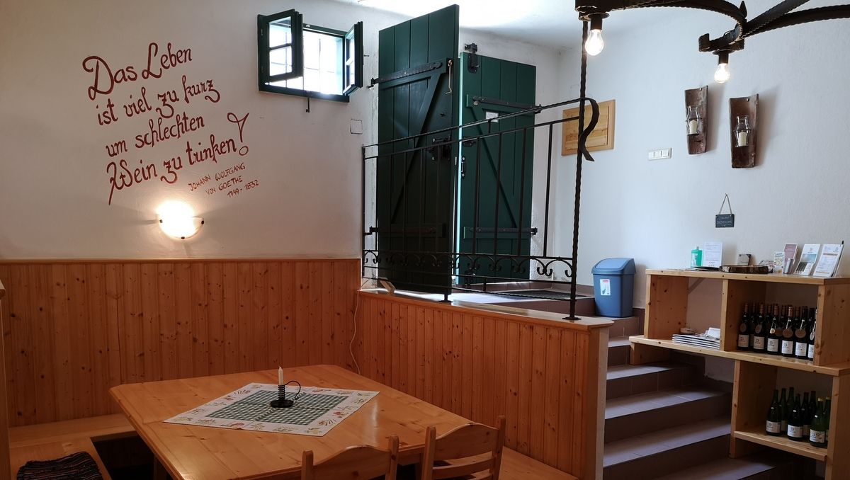 Egy hangulatos borospince belső nézete, fa asztalokkal és polcokkal, a falon Goethe-idézettel díszítve.