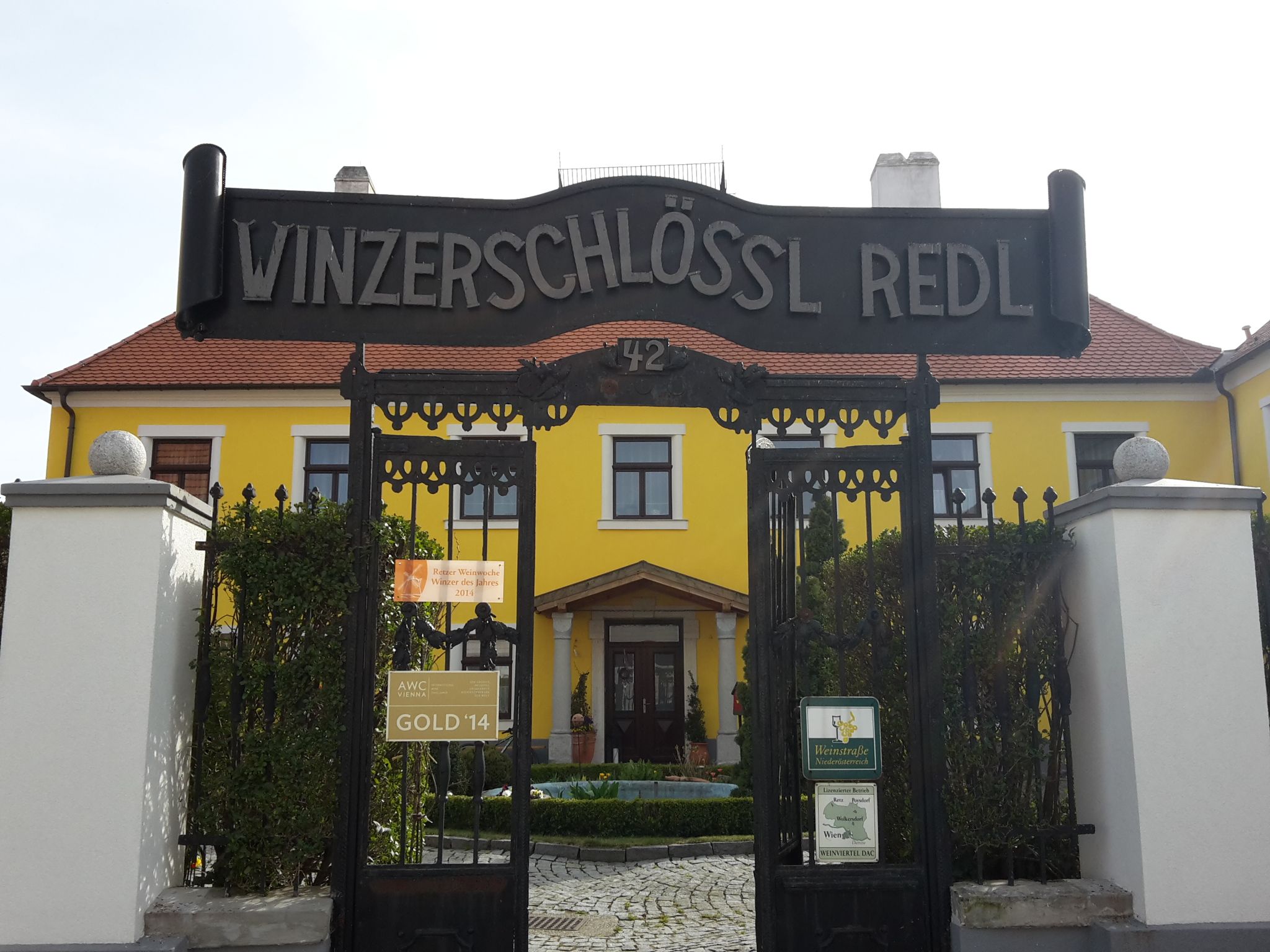 A Winzerschlössl Redl bejárati kapuja, a háttérben sárga épület.