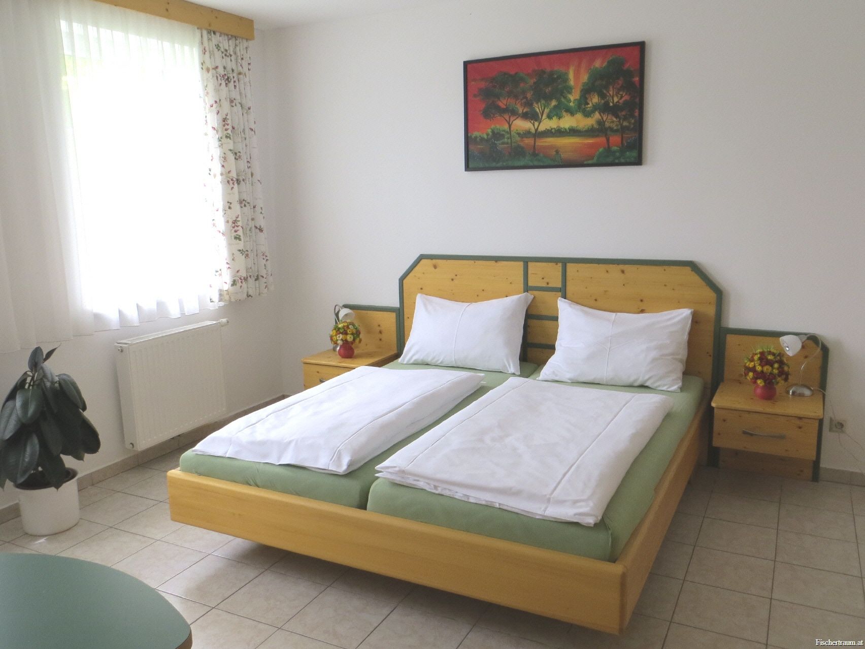 Vendégszoba franciaággyal, éjjeliszekrényekkel, képpel a falon és függönyös ablakkal.