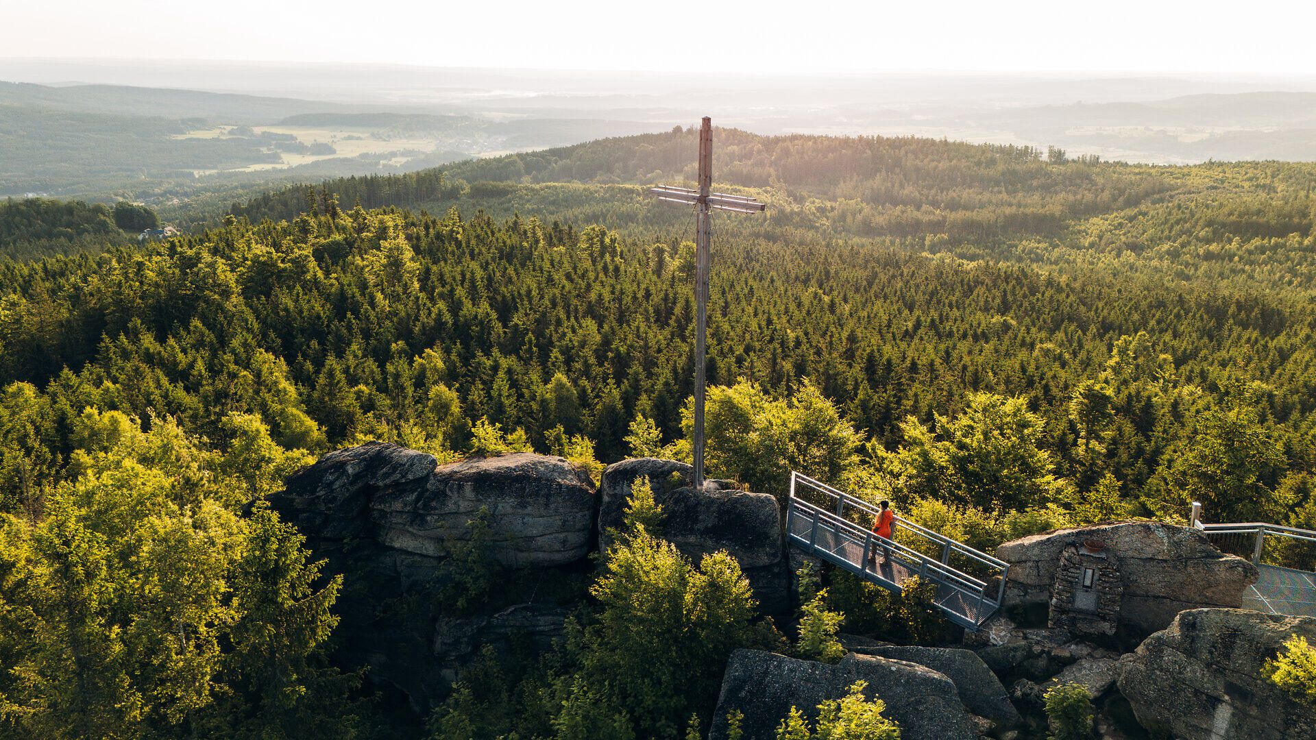 Aussichtsplattform auf einer Felsformation mit Blick über dicht bewaldete Hügel im Waldviertel, unter einem klaren blauen Himmel.
