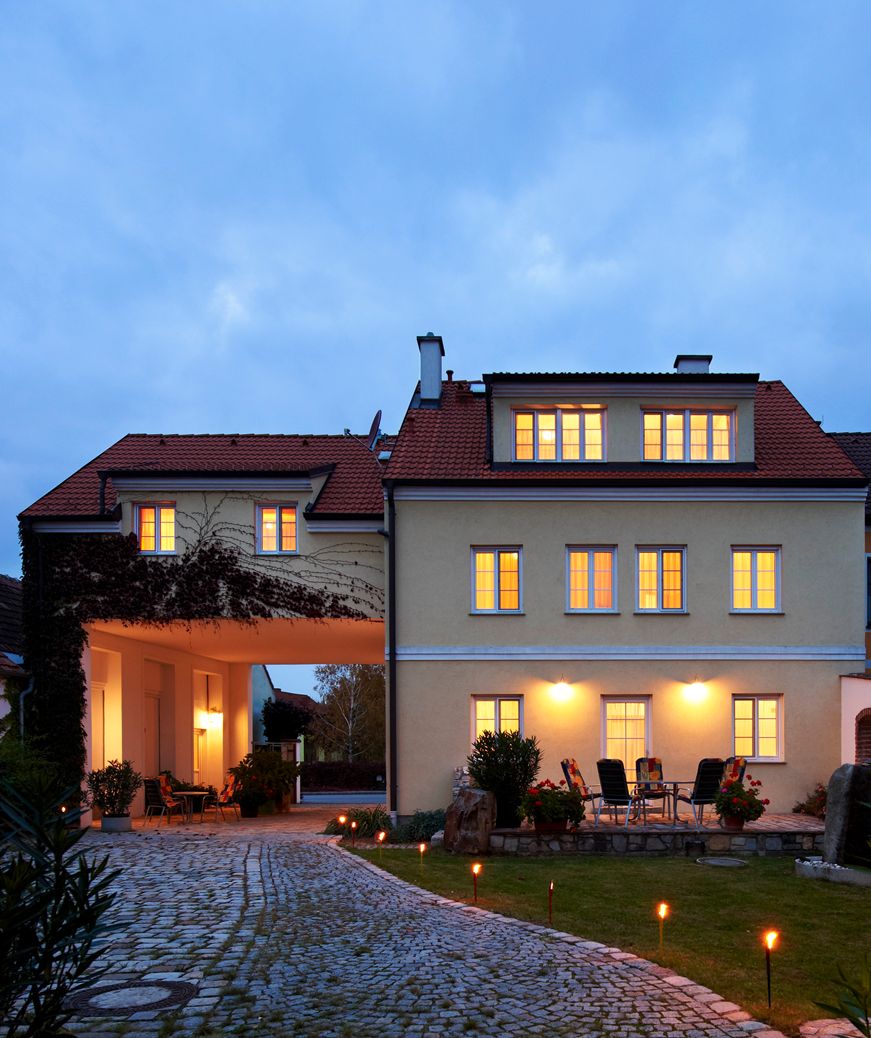 Megvilágított épület, előtérben kövezett út és kerti bútorok.