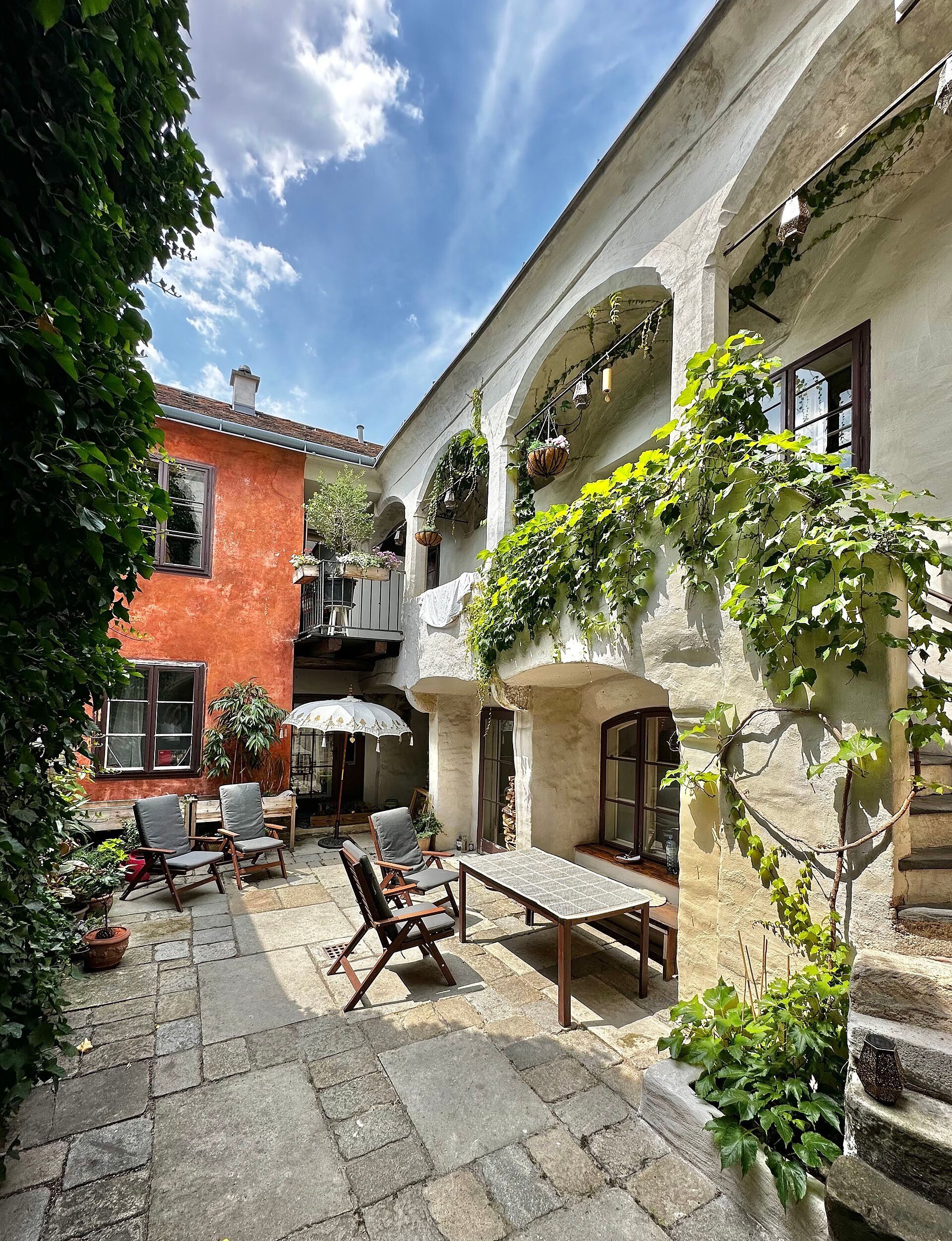 Hangulatos udvar növényekkel, fabútorokkal és napernyővel.