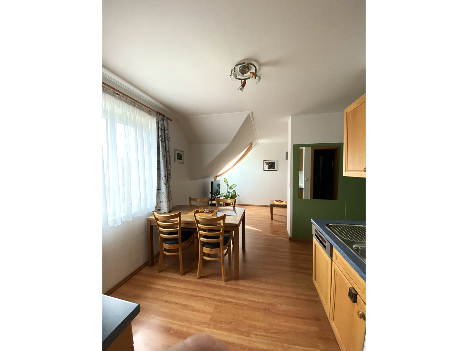 Egy apartman belső nézete étkezőasztallal, székekkel és konyhasarokkal.