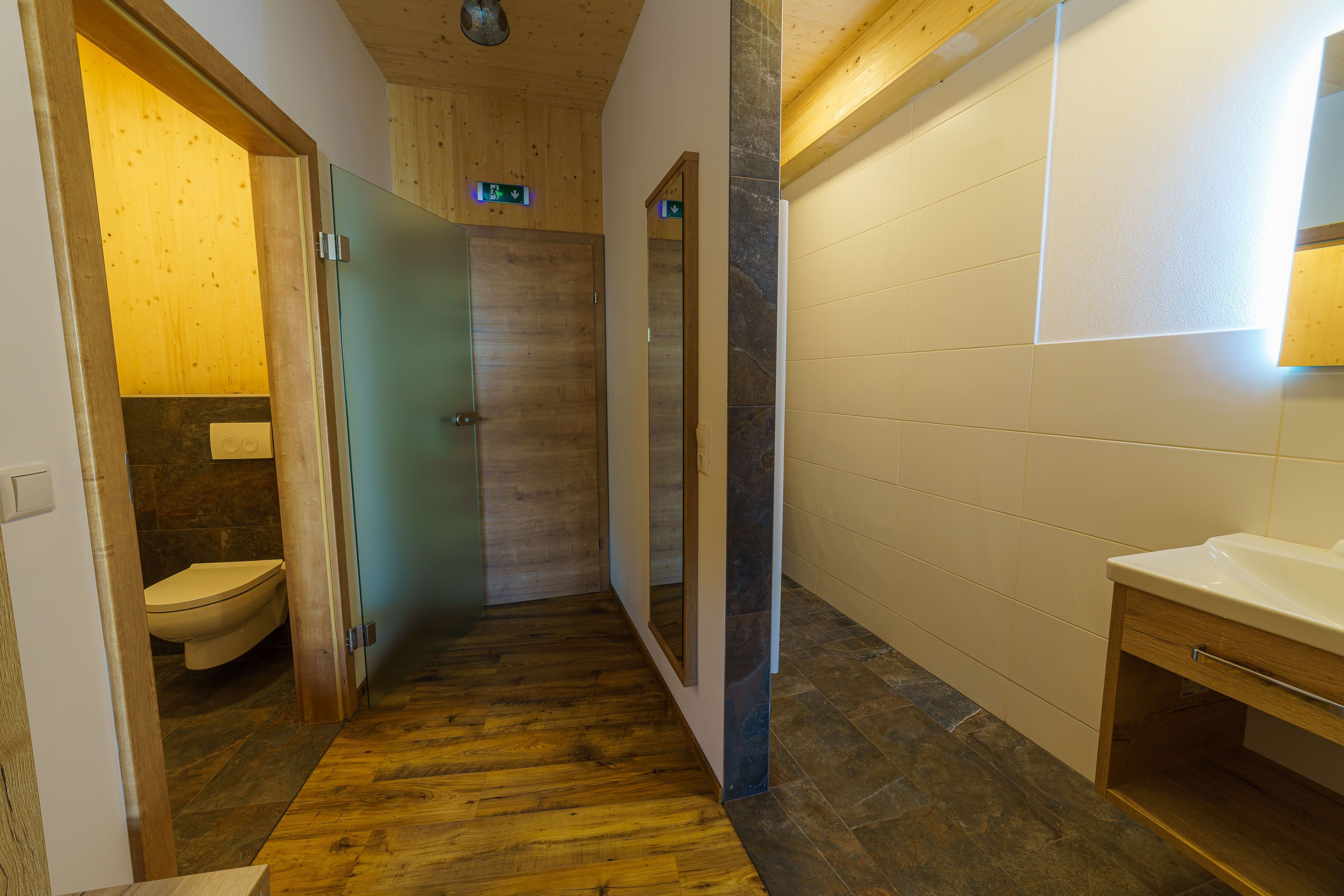 Modern fürdőszoba fa elemekkel és üveg részletekkel.