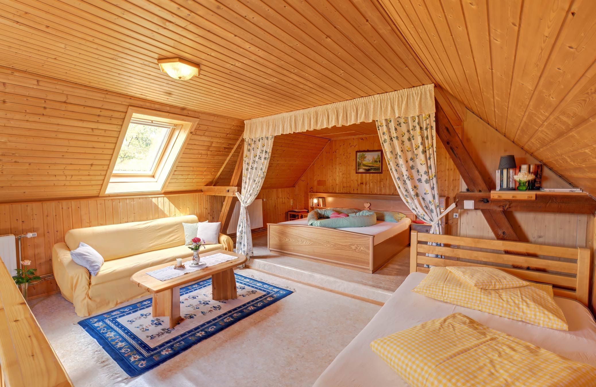 Hangulatos hálószoba fából készült falakkal, ággyal, kanapéval és tetőablakkal.