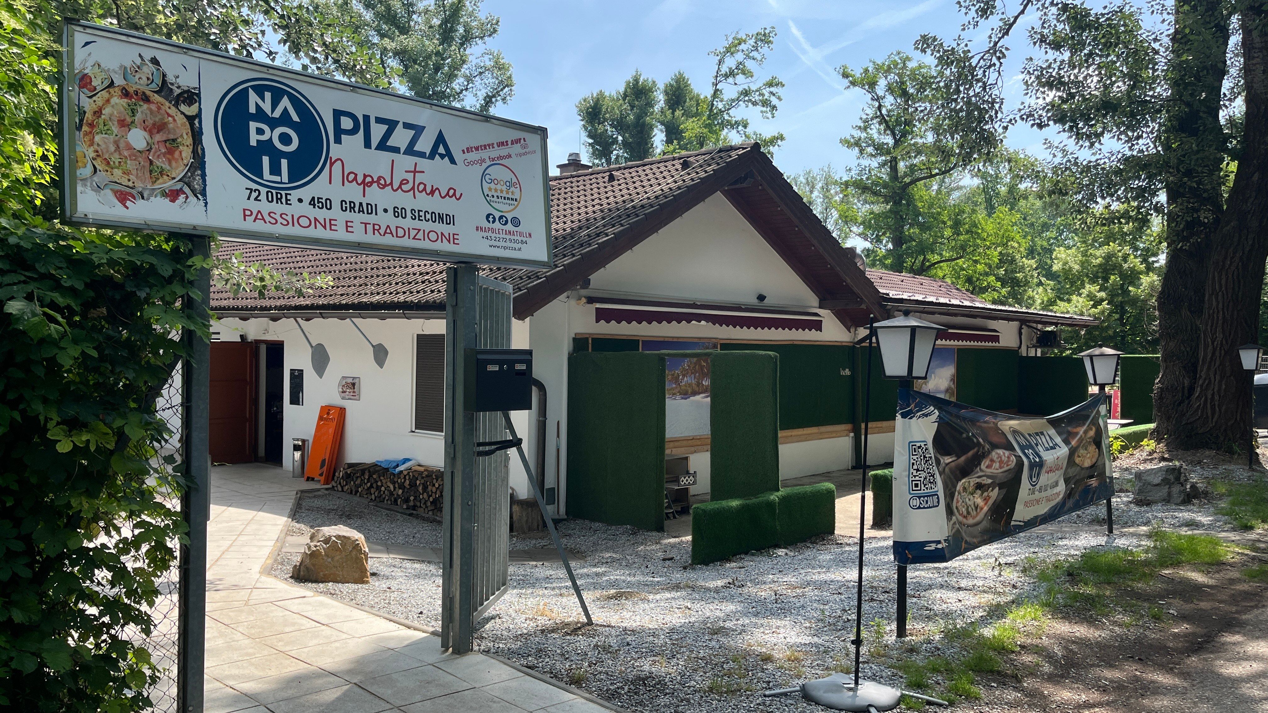 A bejárati terület a parkolóból nézve. Bejárati kapu nagy pizzéria felirattal és lámpákkal.