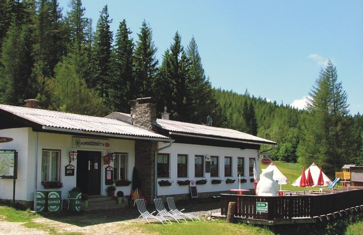 Almrausch kunyhó erdei tájban, napernyőkkel és nyugágyakkal.