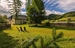 A Wienerbruck-Josefsberg állomáson megáll egy aranyszínű vonat, amelyet zöld vidék és egy kis szabadtéri ülőhely vesz körül.