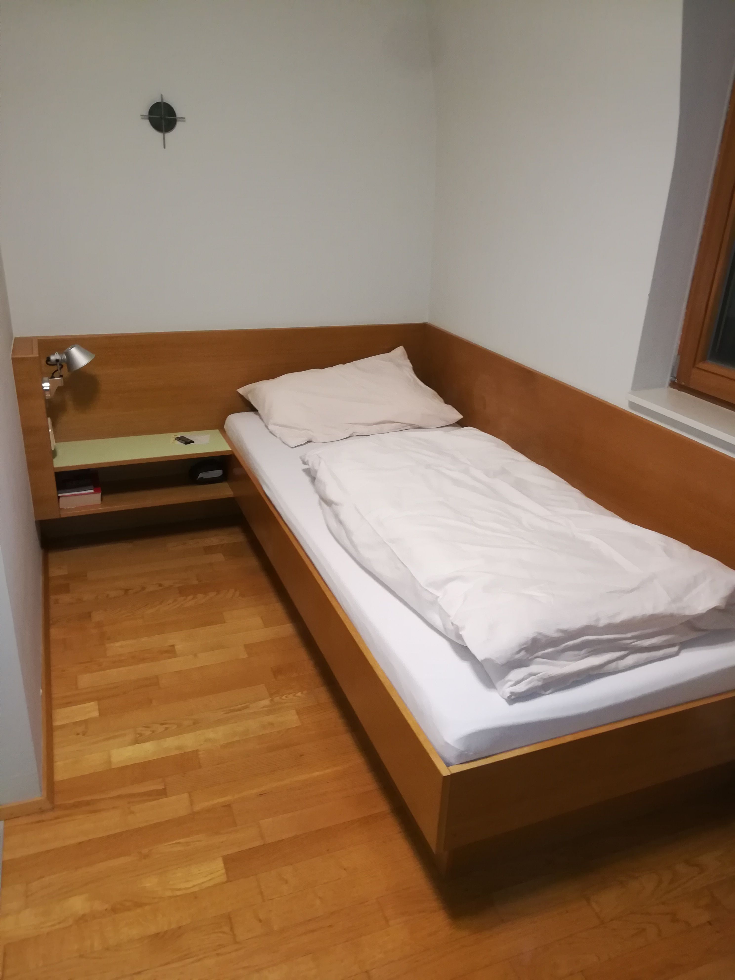 Egyágyas szoba faággyal, éjjeliszekrénnyel és lámpával.