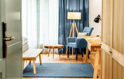 In einem stilvoll eingerichteten Raum mit sanften Farben und warmem Licht lädt ein bequemer Sessel zum Entspannen ein. Die großen Fenster lassen viel Tageslicht herein und bieten einen Blick auf die ruhige Umgebung, während der Holzfußboden eine gemütliche Atmosphäre schafft.