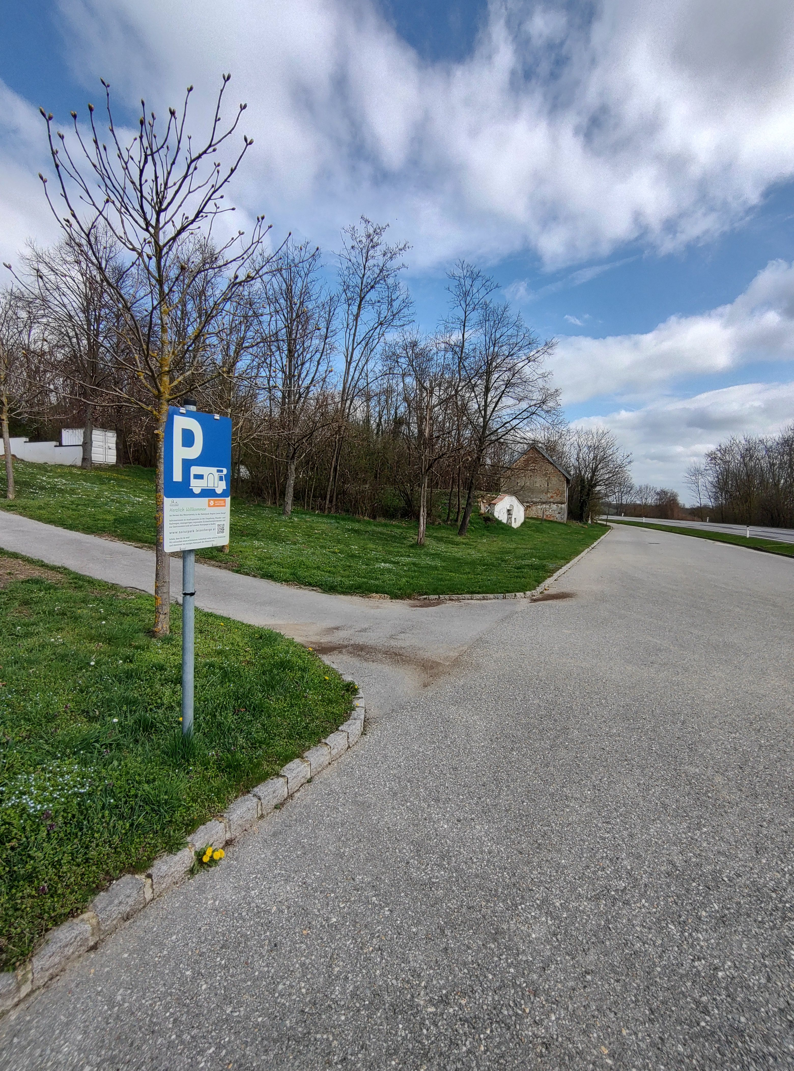 Lakókocsiparkoló, parkolótáblával és fákkal a háttérben.