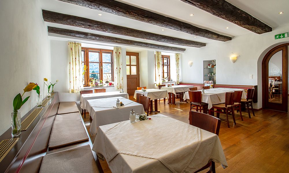 Hangulatos reggelizőterem fagerendákkal, terített asztalokkal és virágokkal az ablakpárkányokon.