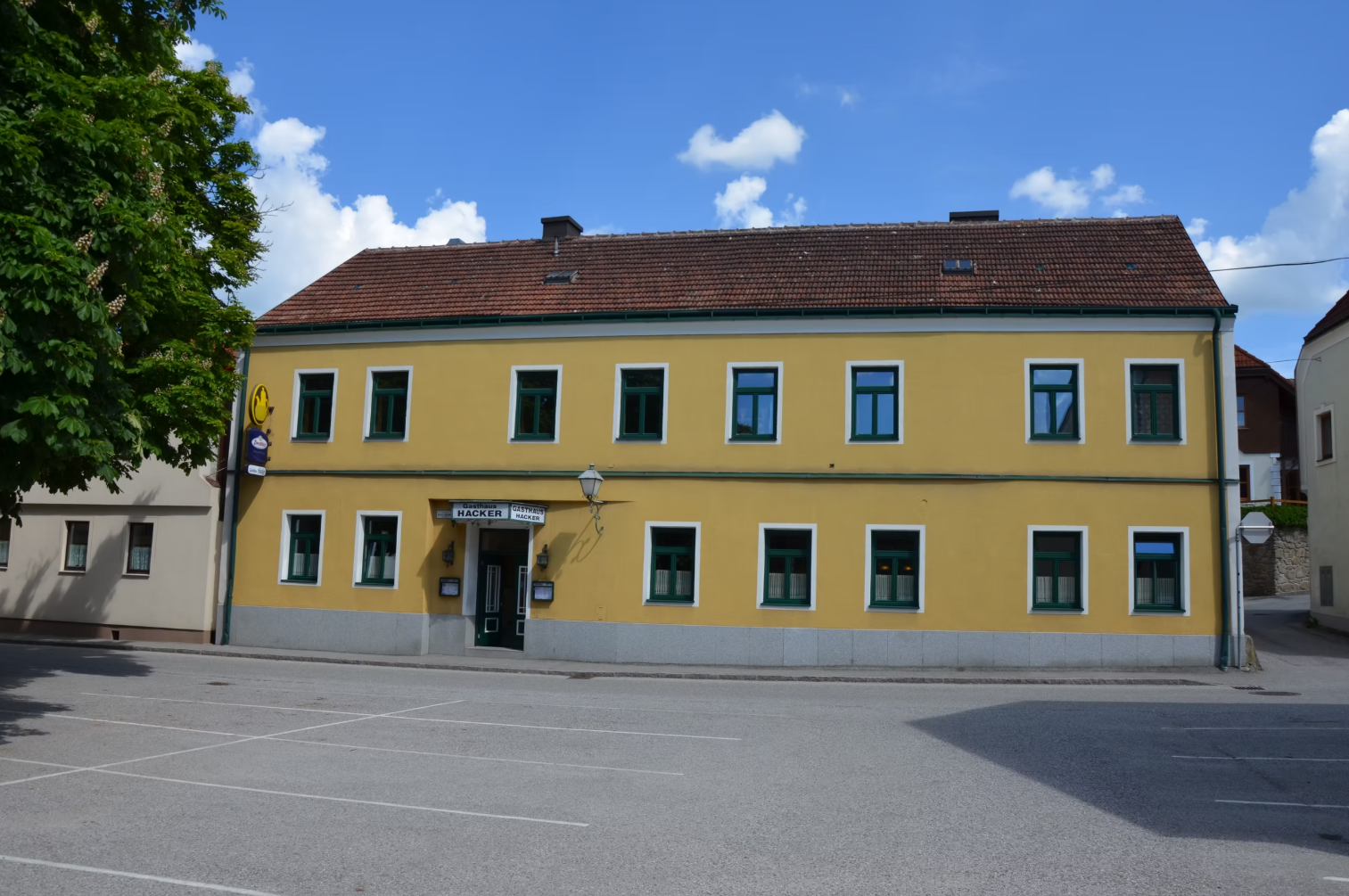 Sárga kétszintes épület, zöld ablakkeretekkel és "Gasthaus Georg Hacker" feliratú táblával.