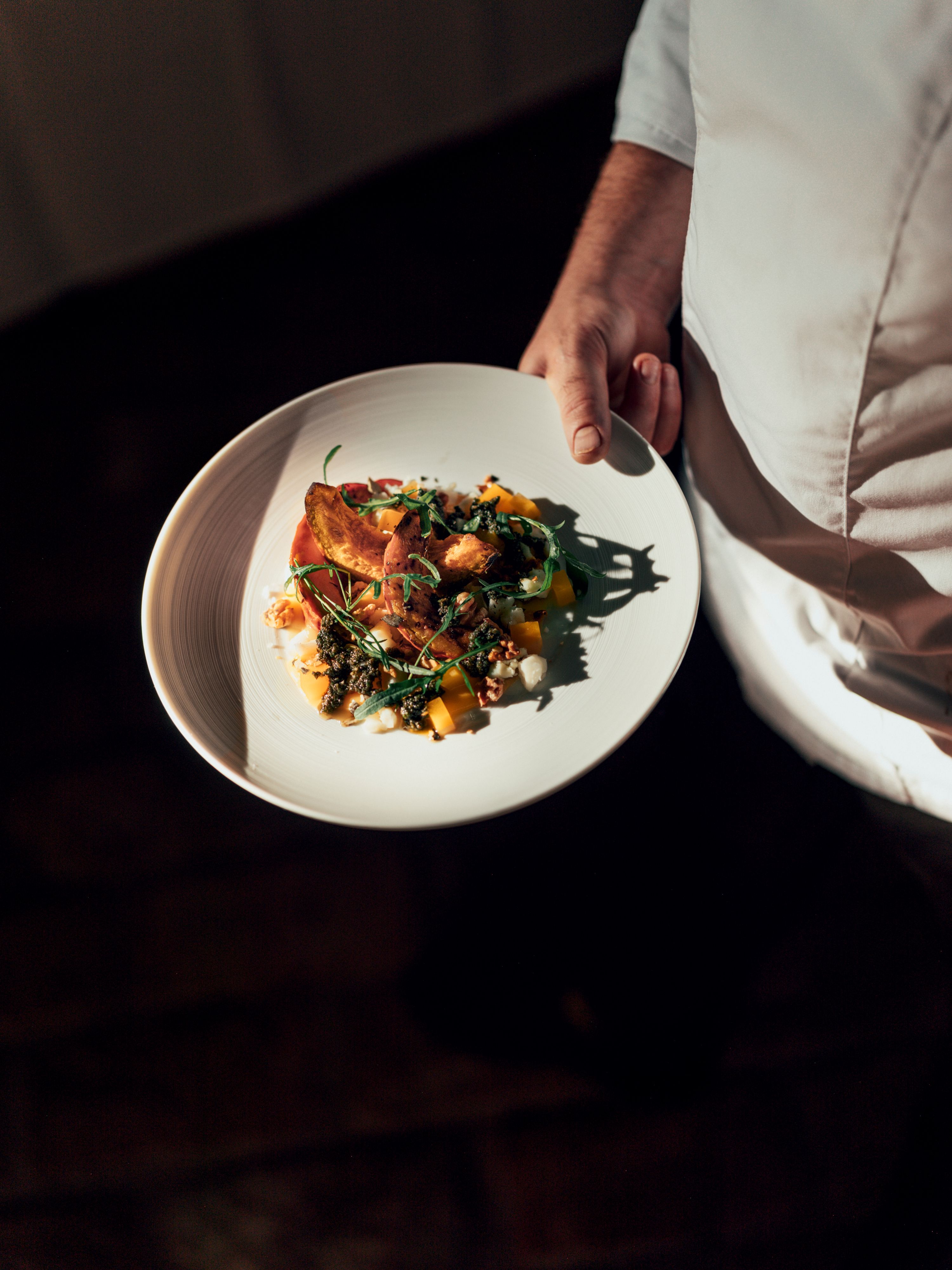 Egy fehér ruhás személy egy tányért tart a kezében, amelyen egy díszesen elrendezett tál van.