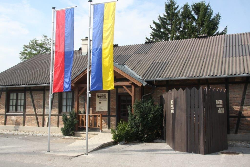 A Strasshof helytörténeti múzeum bejárata két zászlórúddal és fakerítéssel.