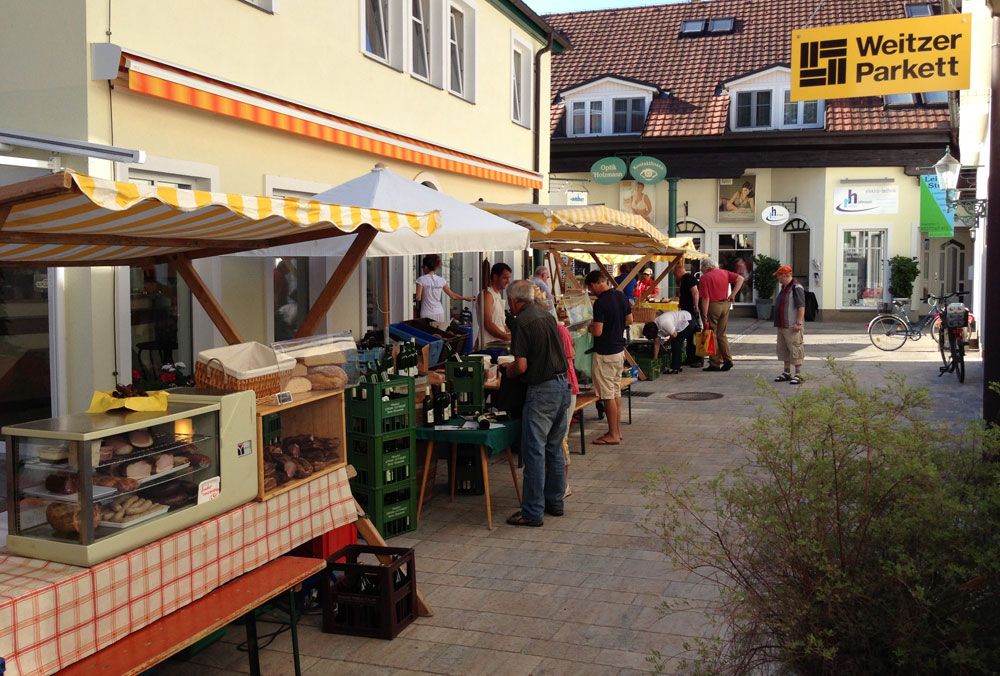 Őstermelői piac egy átjáróban, bódékkal és látogatókkal.