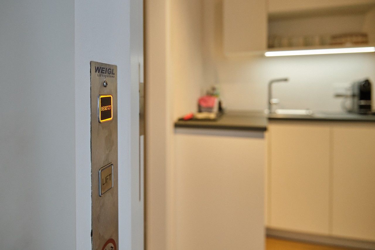 A konyha melletti modern nappaliban világít egy "Busy" feliratú liftgomb.