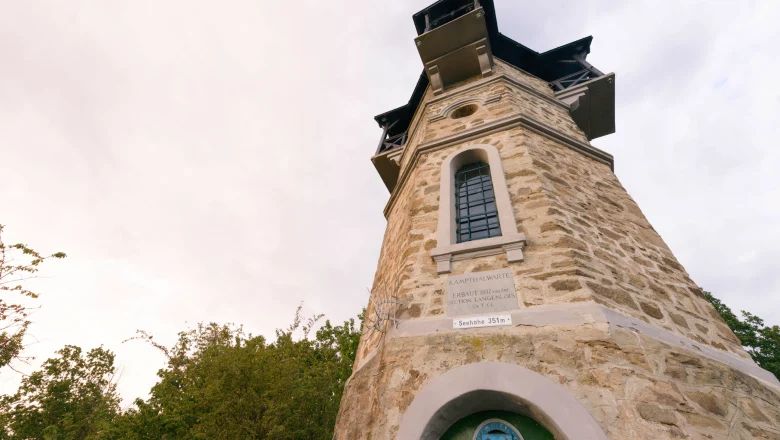 Fákkal körülvett, ablakokkal és felirattal ellátott kő kilátótorony.