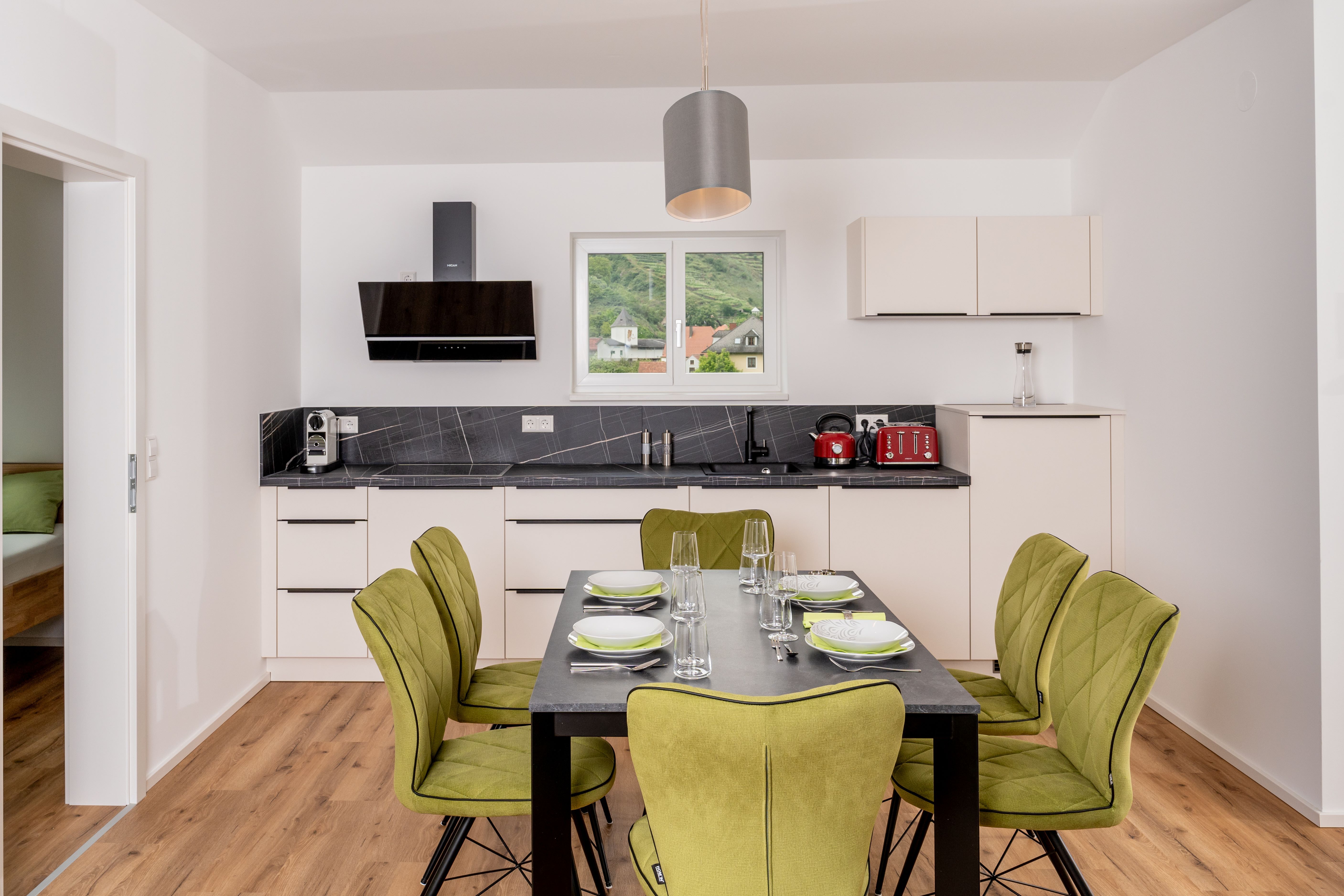 Modern konyha étkezőasztallal és zöld székekkel, ablak a hegyekre néző kilátással.