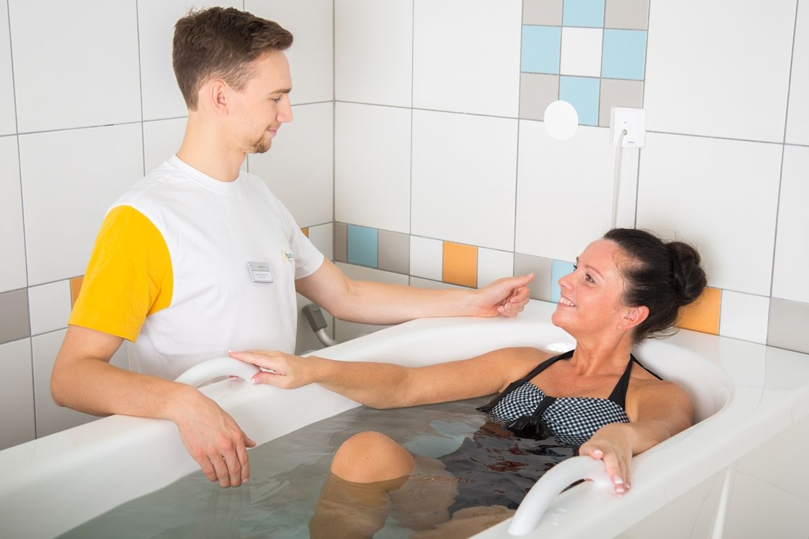 Egy kénes fürdőben lévő nőre egy terapeuta vigyáz.