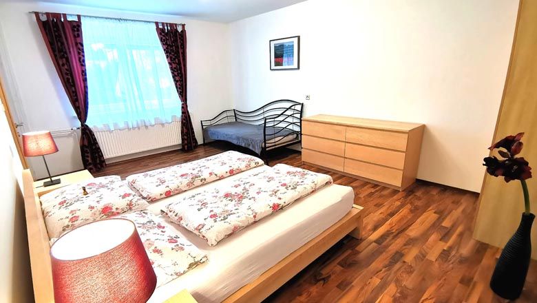 Hálószoba franciaággyal, egyszemélyes ággyal, komóddal és virágokkal vázában.