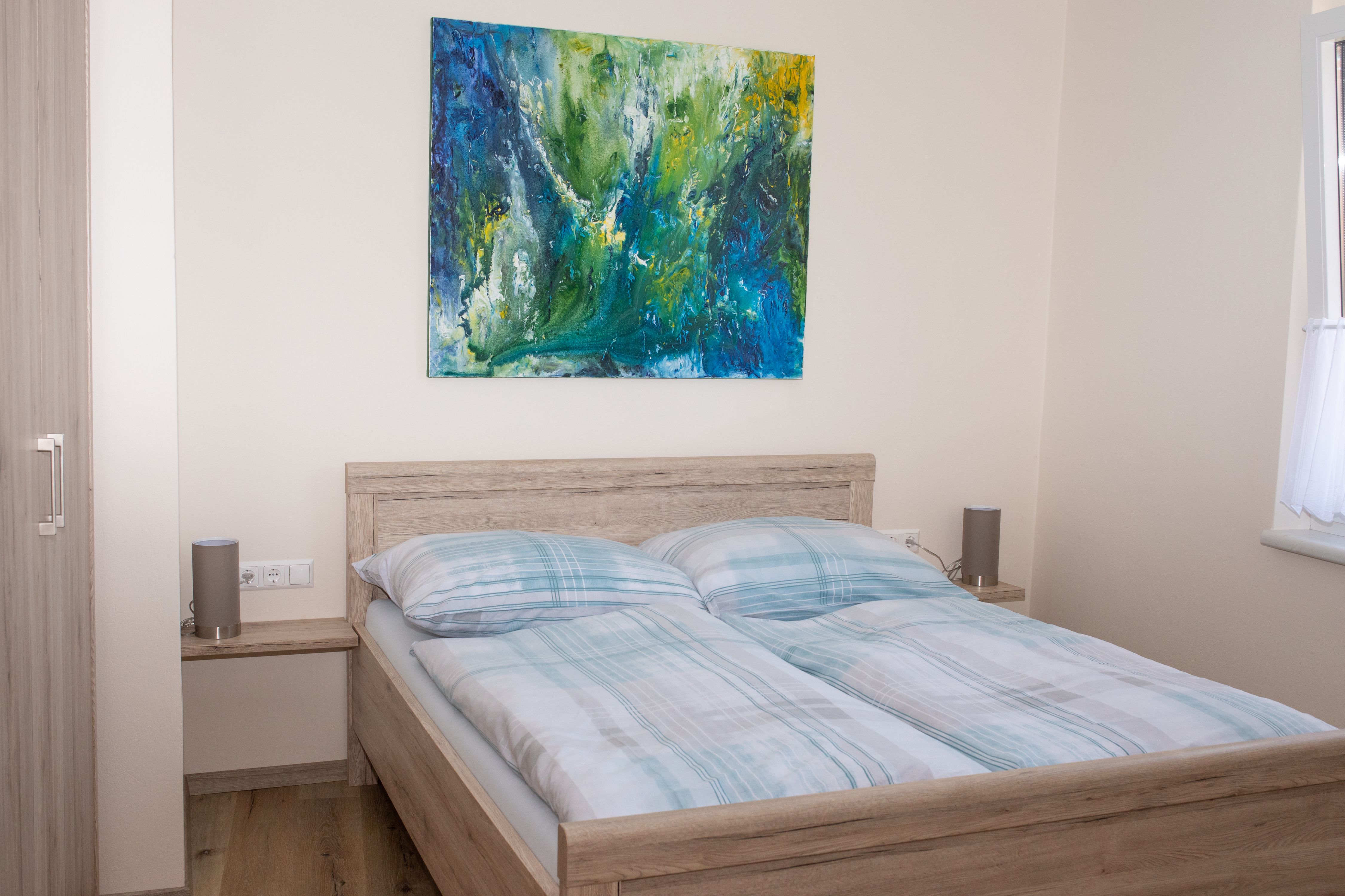 Hálószoba franciaággyal, absztrakt festménnyel a falon és függönyös ablakkal.