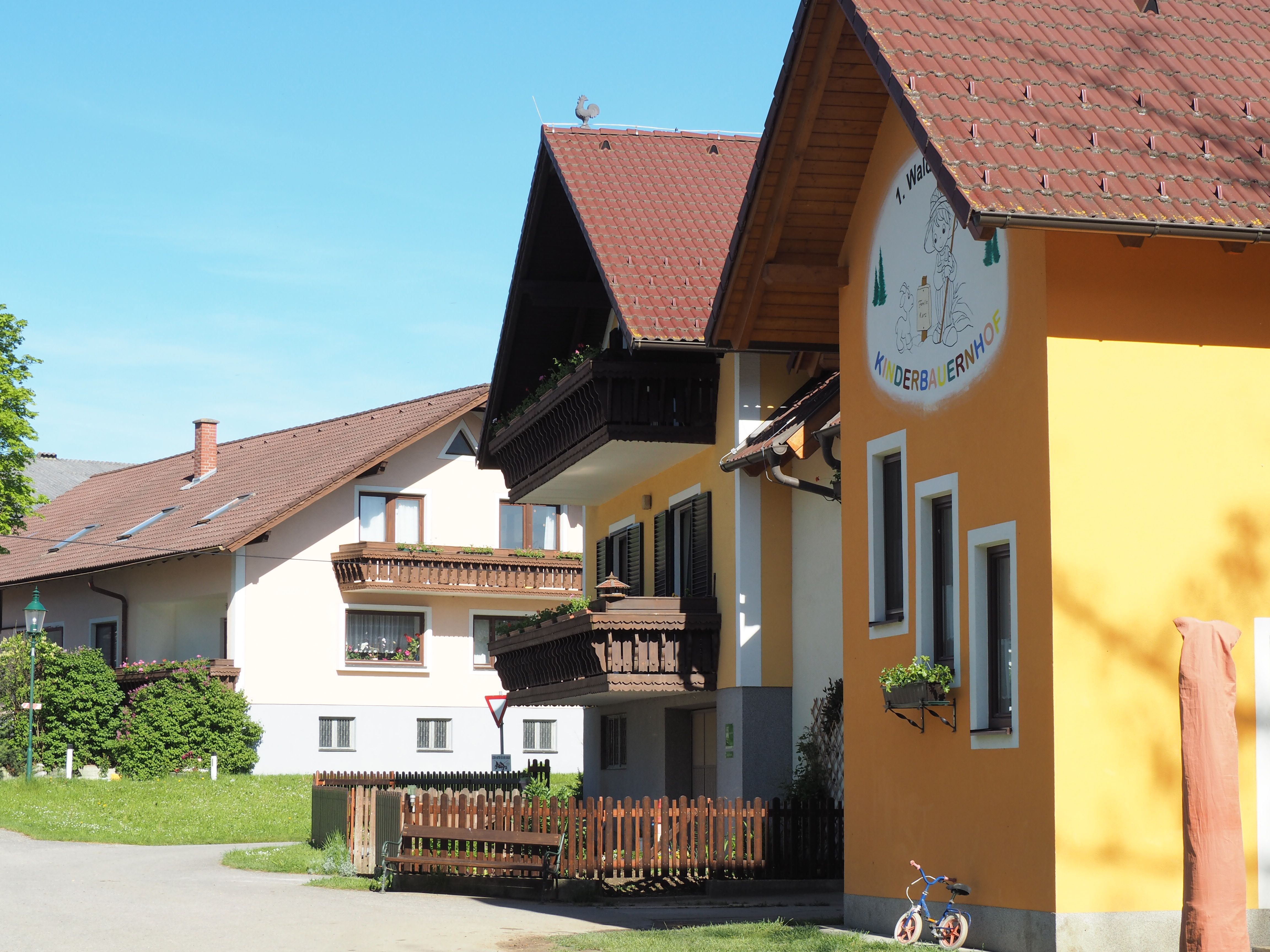 Waldviertel gyermekfarm épülete sárga homlokzattal és fa erkélyekkel, zöld vidékkel körülvéve.