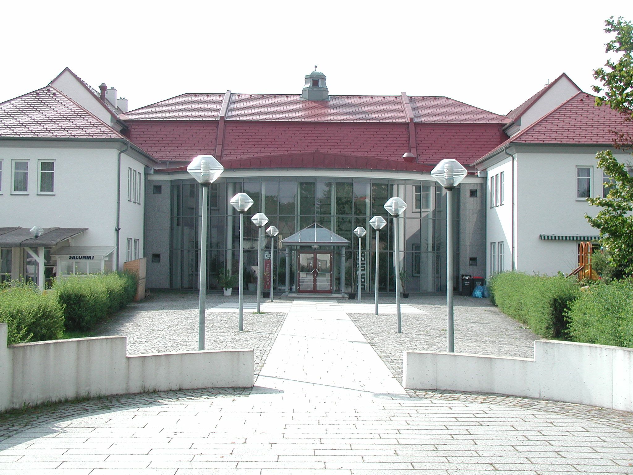 Egy modern kulturális központ bejárata üveghomlokzattal és vörös tetővel.