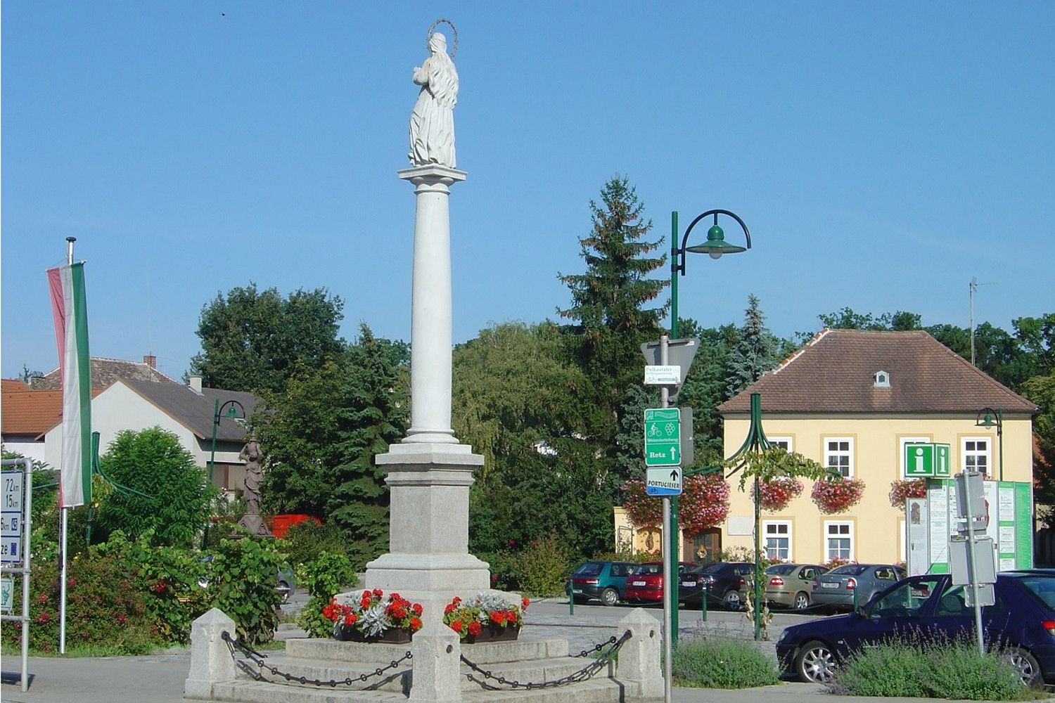 Szobor egy oszlopon Haugsdorf egyik terén, épületekkel és fákkal körülvéve.