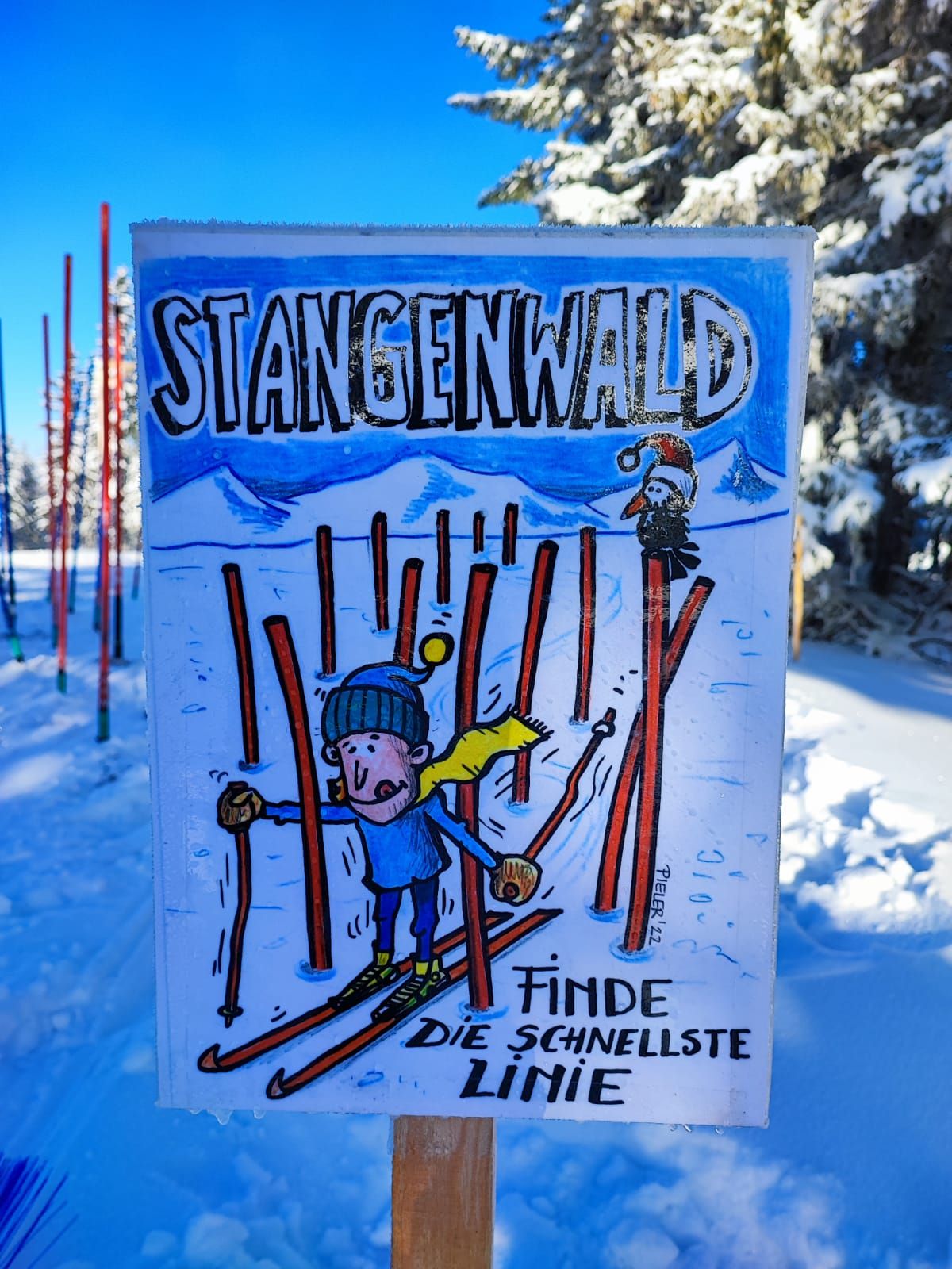Felirat a hóban, rajzfilmfigurával sílécen és a "Stangenwald, találd meg a leggyorsabb vonalat" szöveggel.