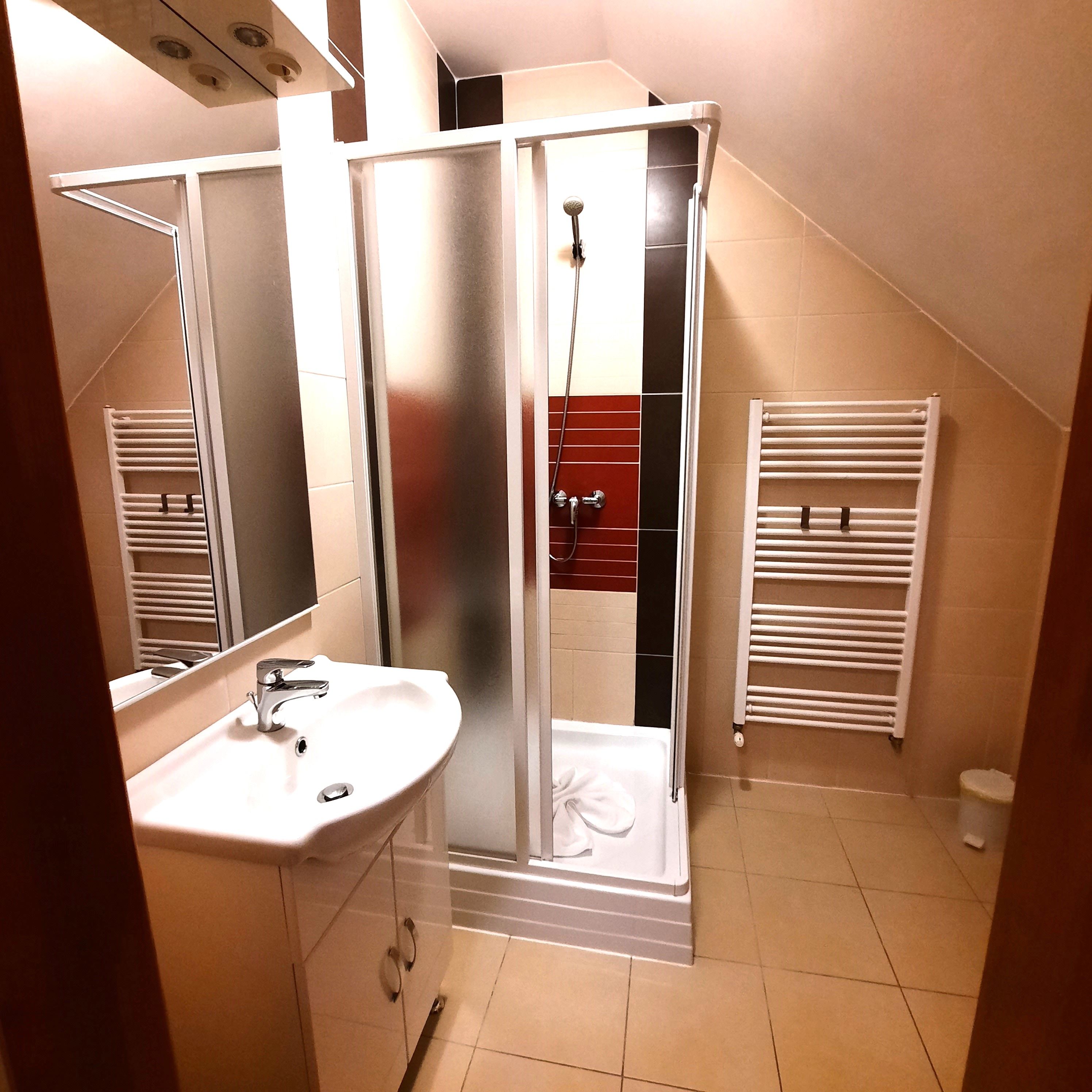 Modern fürdőszoba zuhanyzóval, mosdóval és törölközőradiátorral.