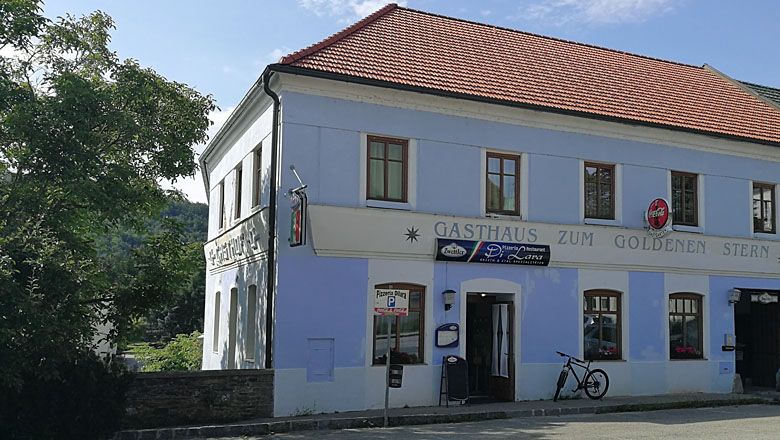 Egy kétszintes épület "Gasthaus zum Goldenen Stern" felirattal és egy kerékpárral előtte.
