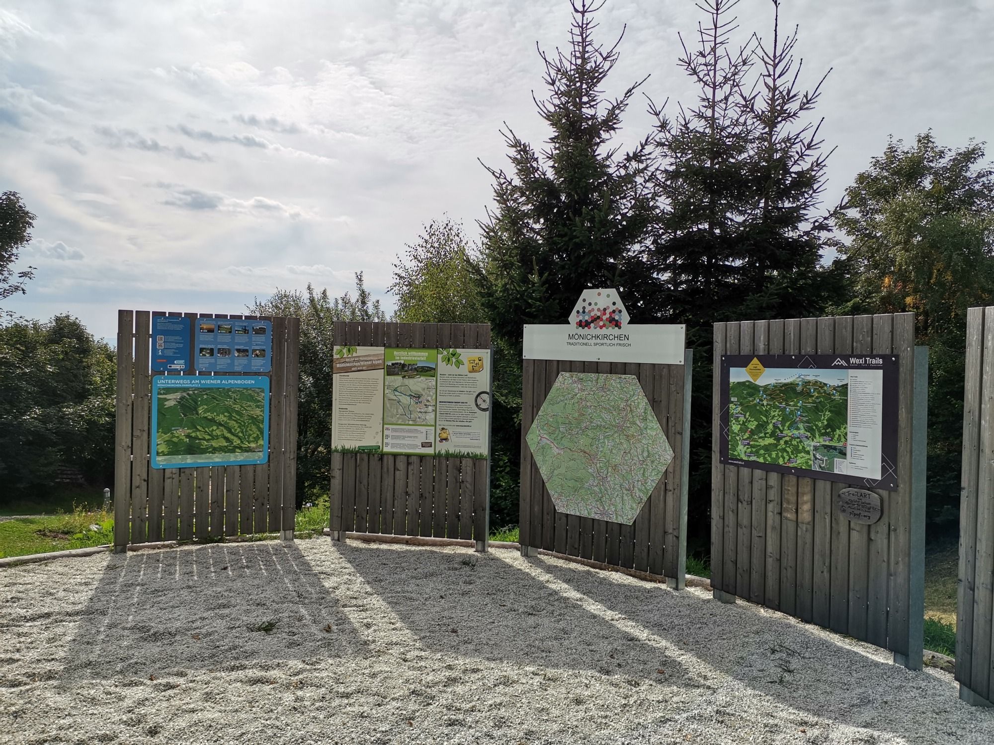 A mönichkircheni túra kiindulópontjánál információs táblák térképekkel és információkkal, fákkal körülvéve.