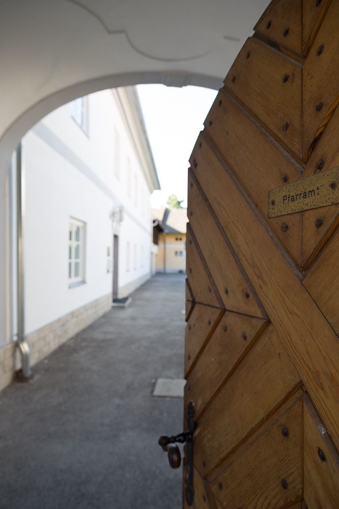 A "Pfarramt" feliratú fakapu egy fehér épületekből álló udvarra nyílik.