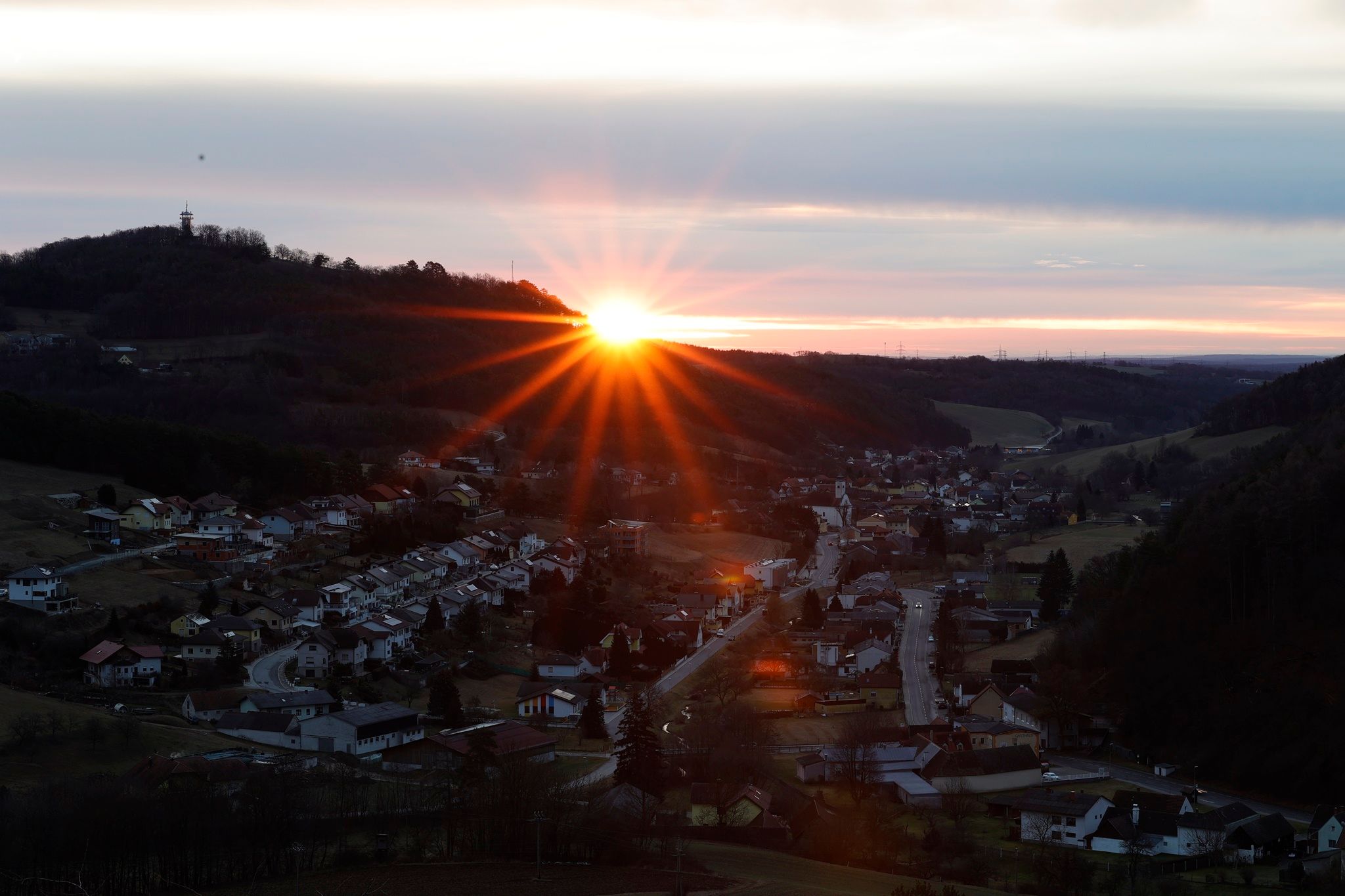 Napfelkelte egy domb mögött, előtérben egy faluval.